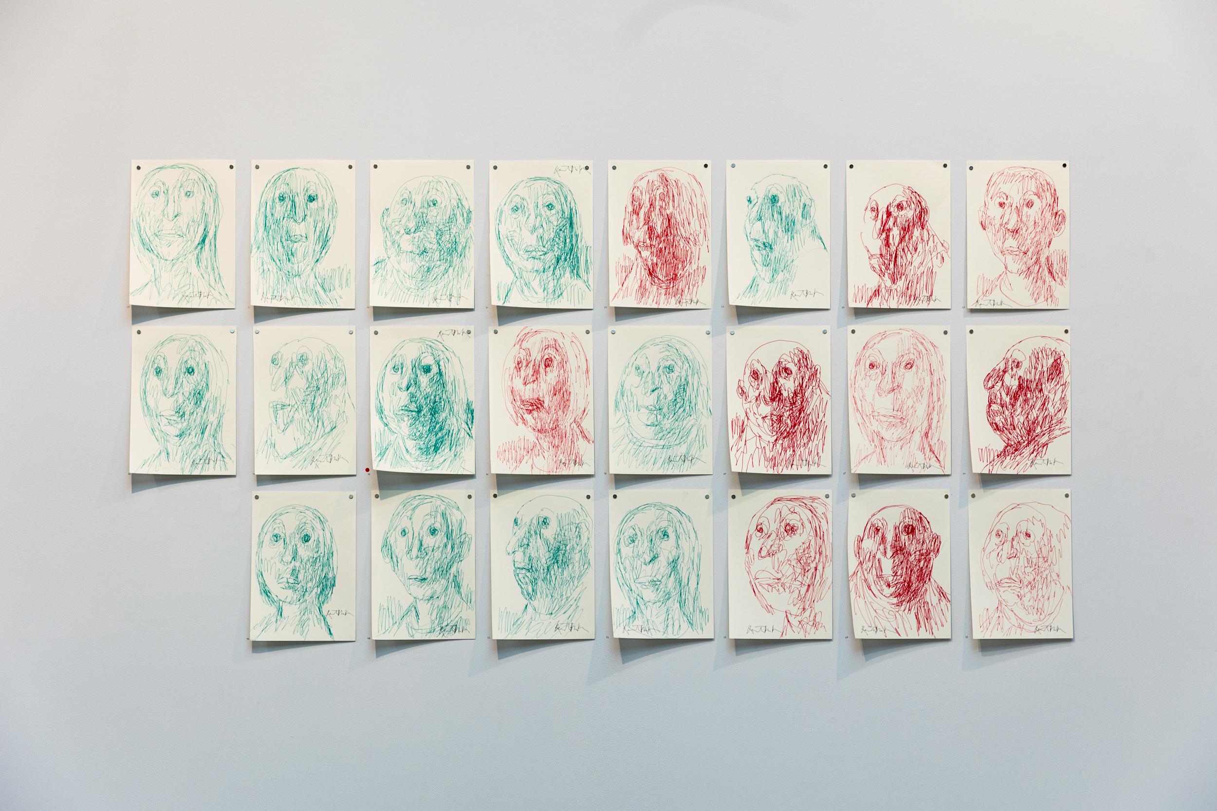 A series of biro illustrations of people's heads in greens and reds pinned to a wall.