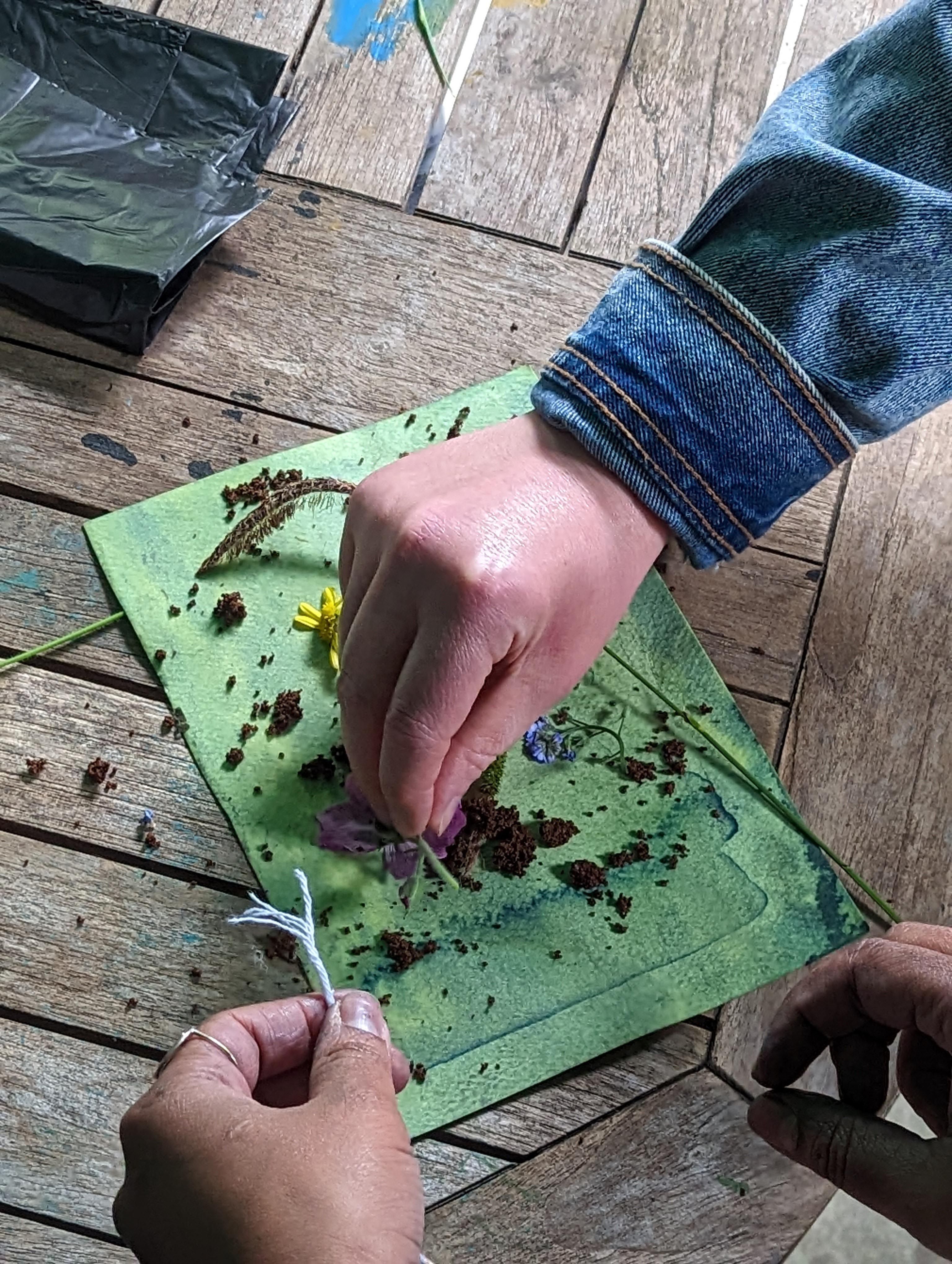 Three hands adding flowers and soil on top of a piece of fabric.