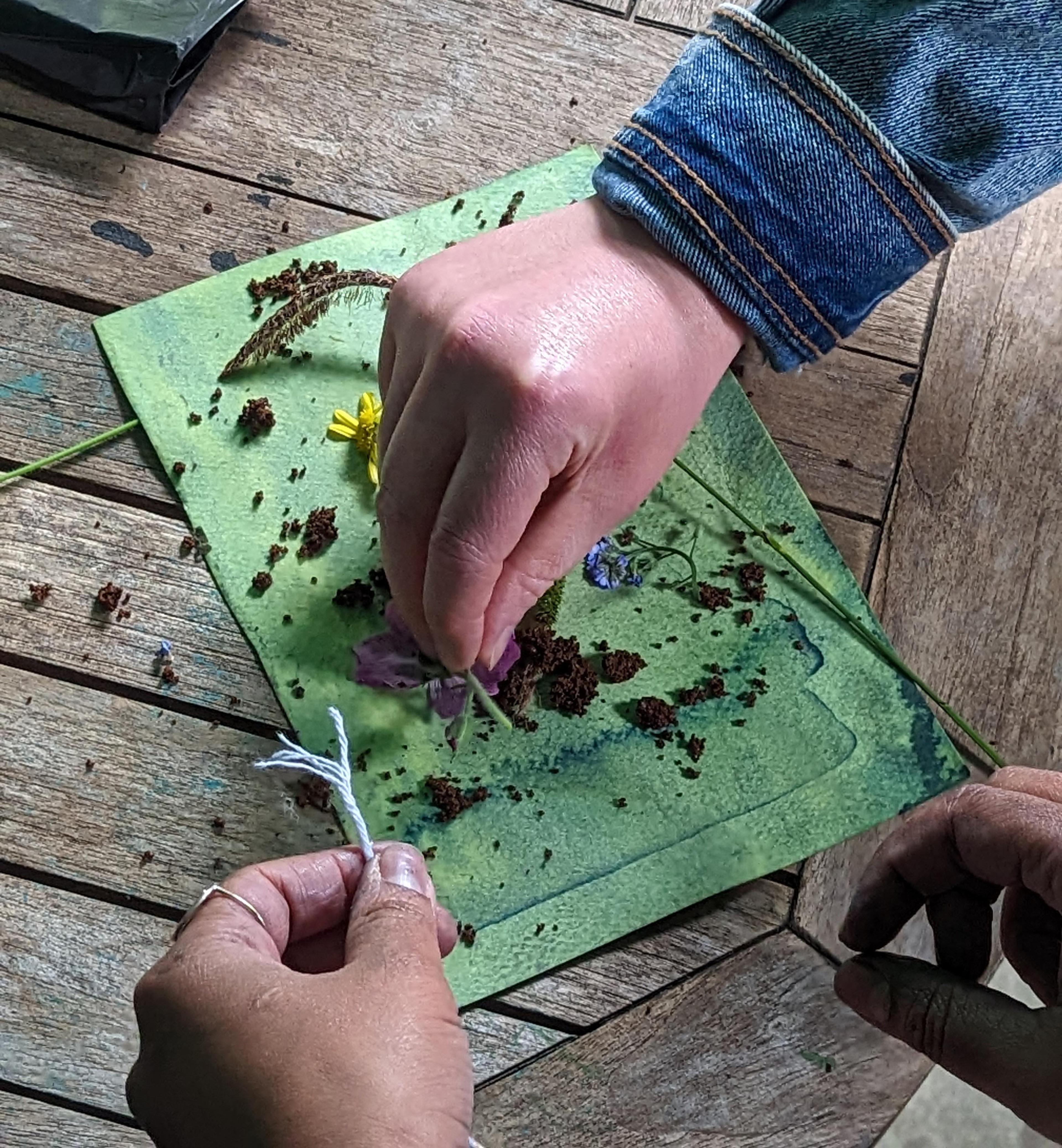 Three hands adding flowers and soil on top of a piece of fabric.