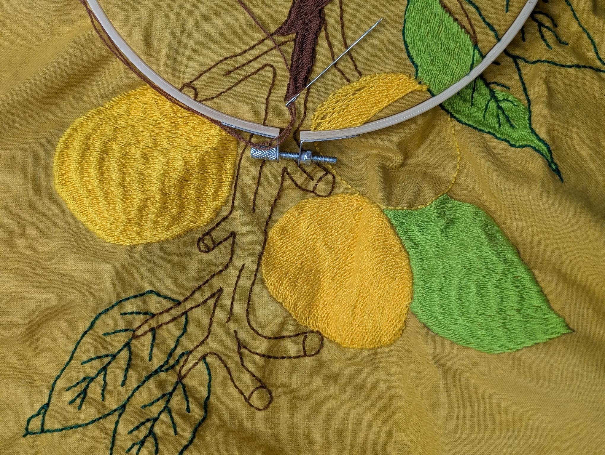 An embroidery hoop over a work in progress featuring an embroidered lemon branch.