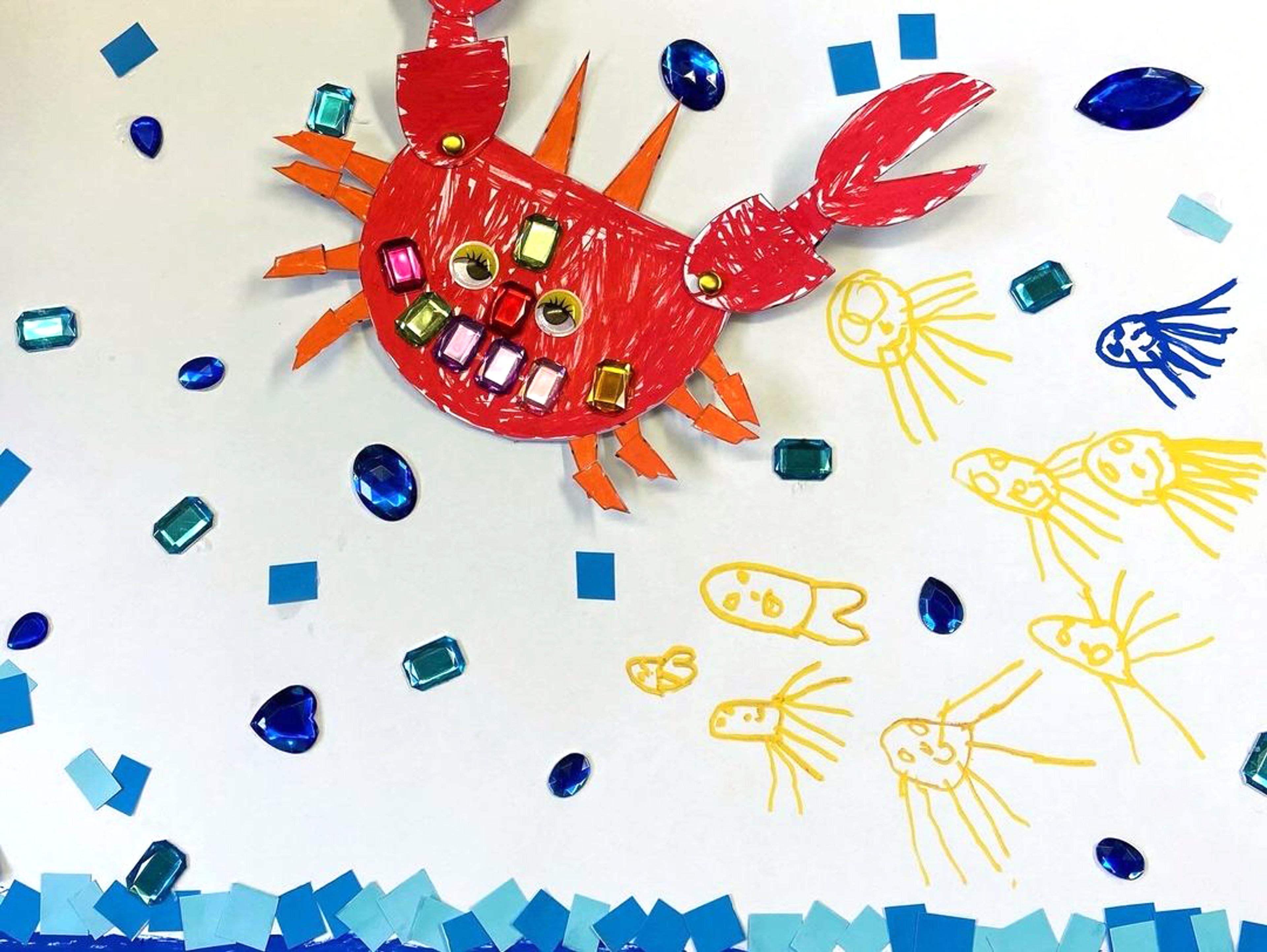 A collage of a red crab, blue waves and yellow jellyfish with artificial jewels, coloured paper and pen