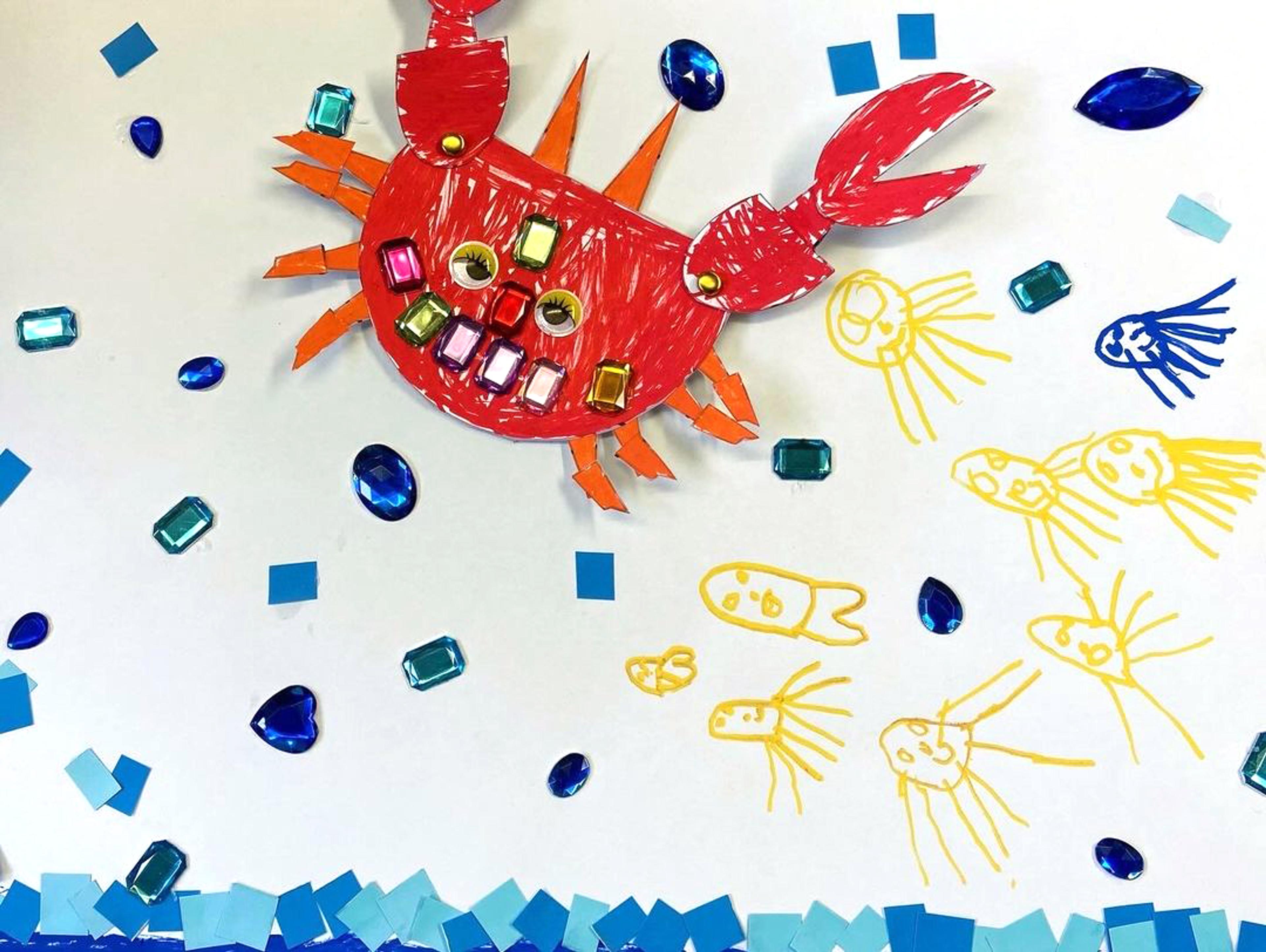 A collage of a red crab, blue waves and yellow jellyfish with artificial jewels, coloured paper and pen