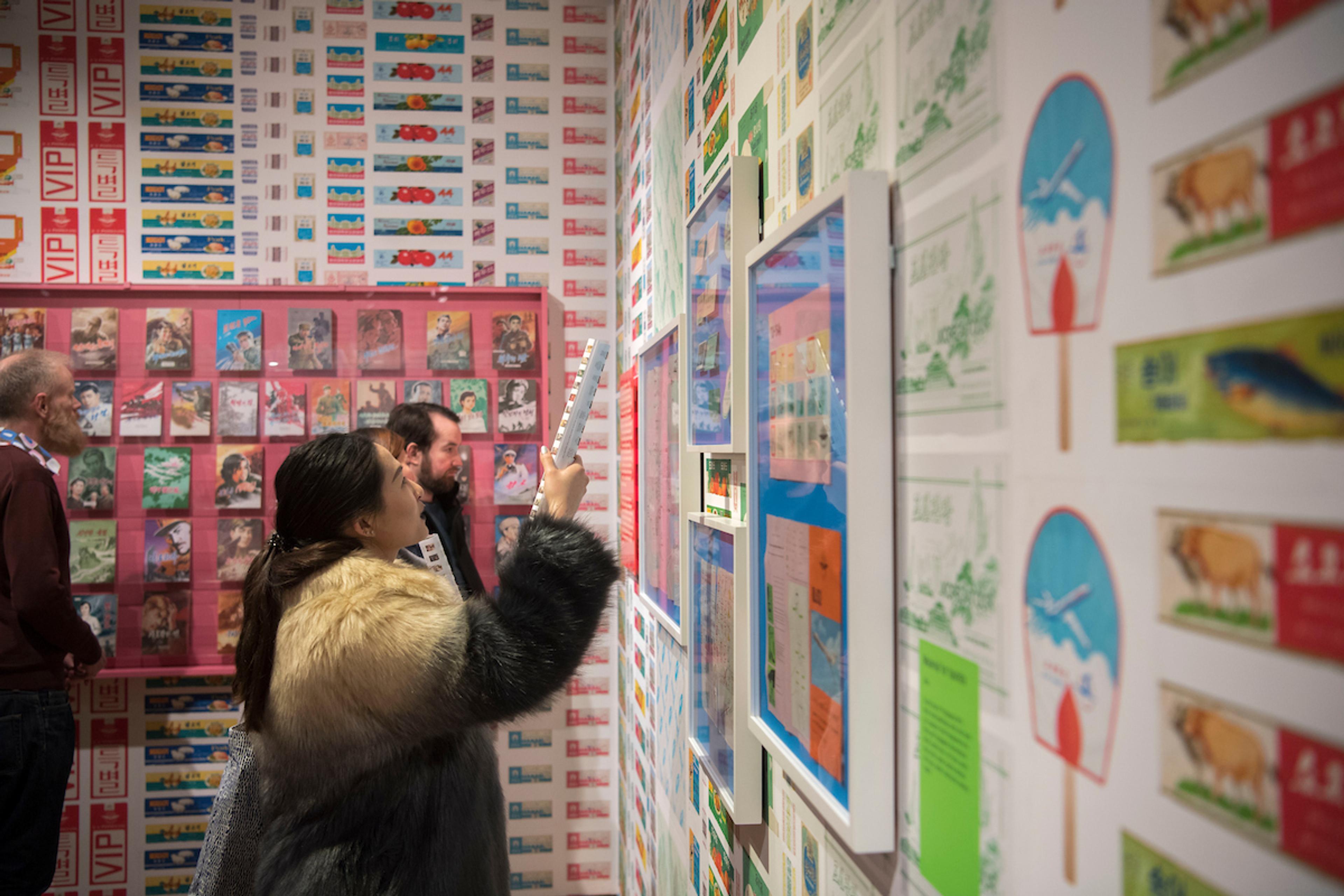 Person in furry jacket holds exhibition guide up to framed artwork