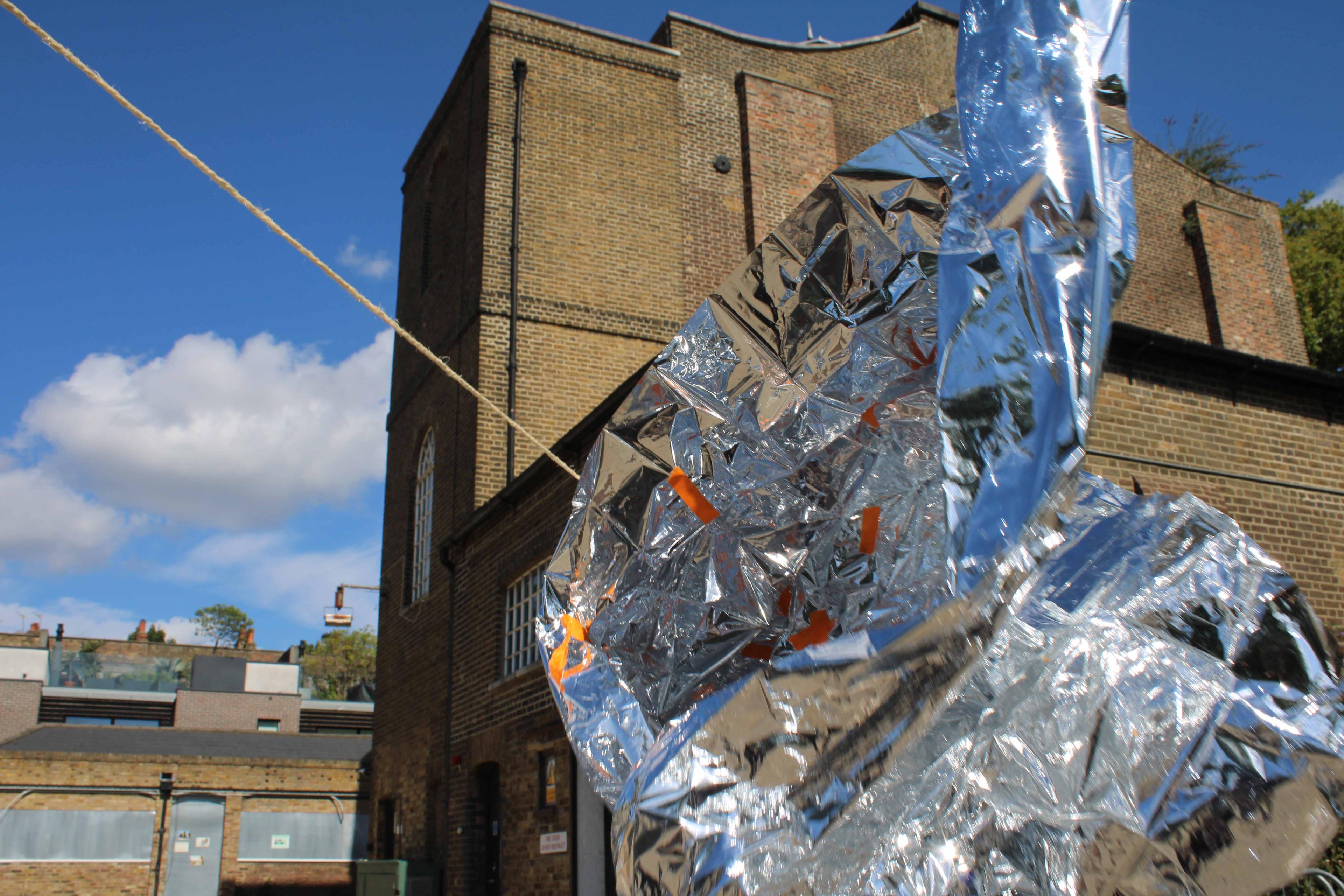 A foil sculpture up close to the camera with brick heritage buildings in the background.