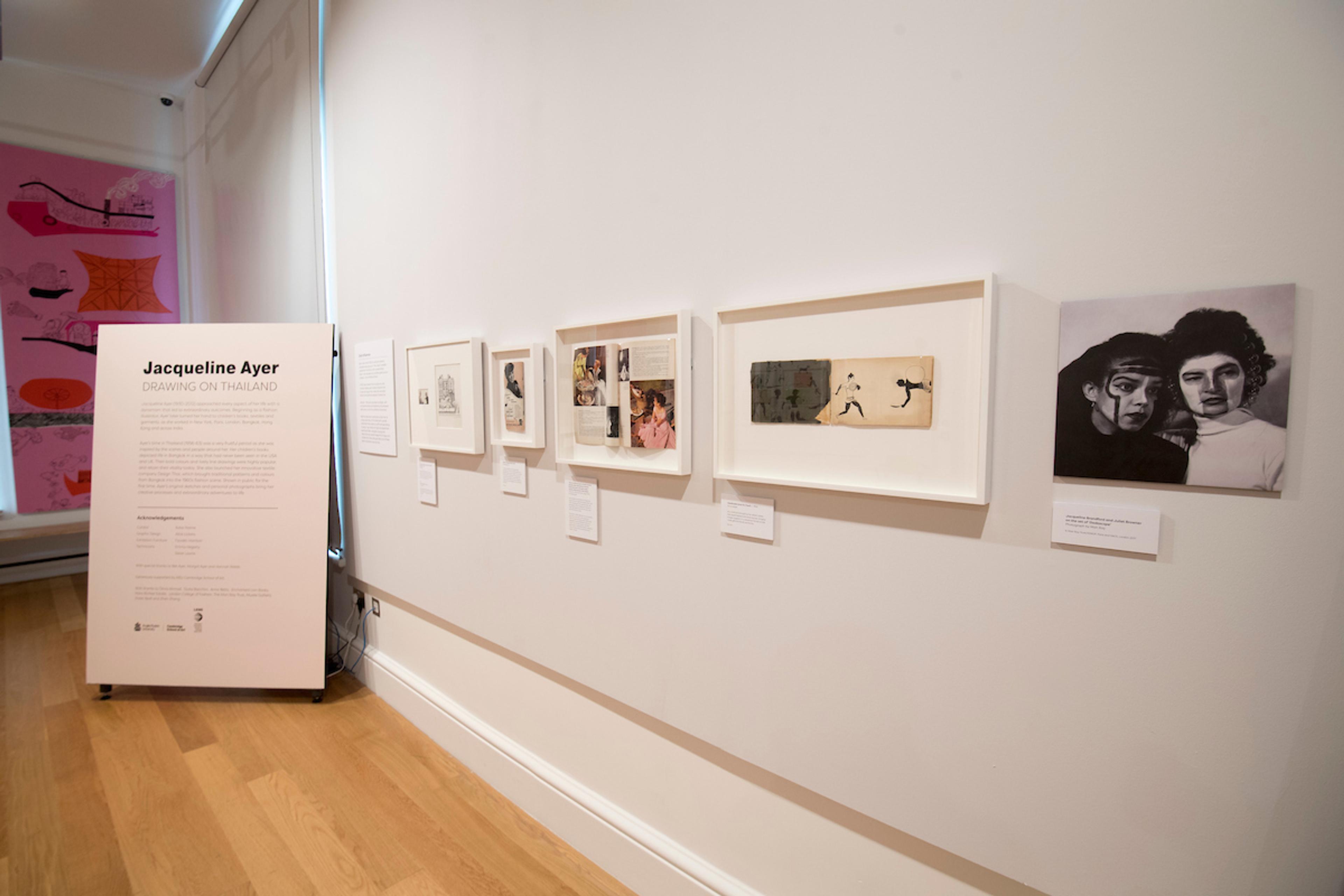 Framed illustrations displayed on a gallery wall with a text display.