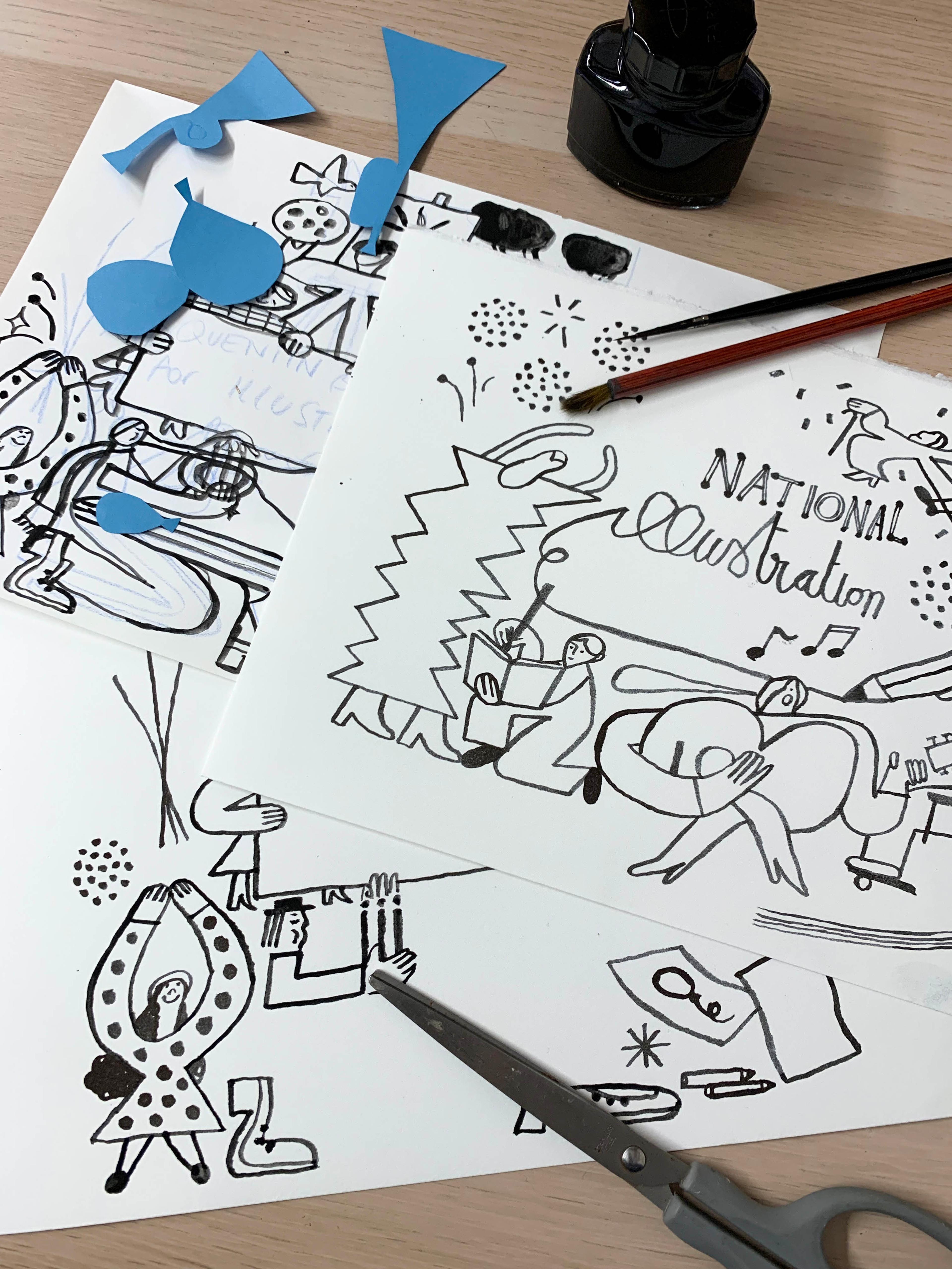 Black and white illustrations on a table surrounded by paint brushes, paper cut outs and scissors.