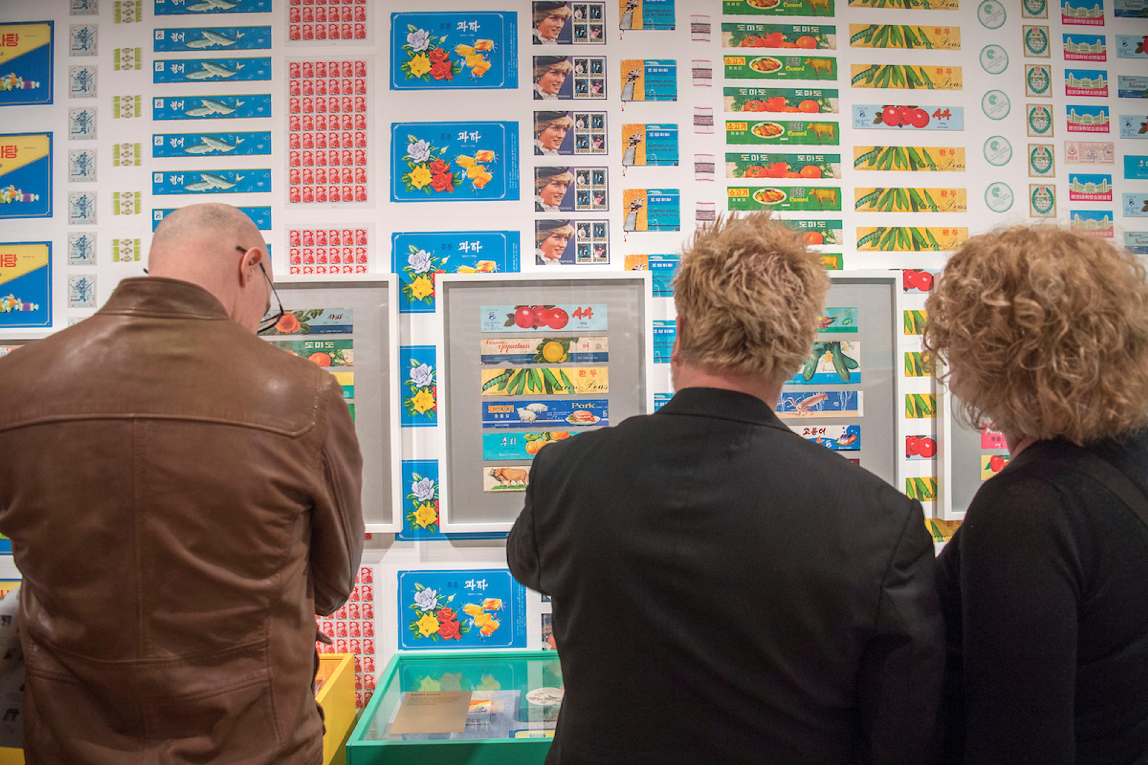 Visitors admiring a framed artwork mounted on a bold wall featuring North Korean graphics