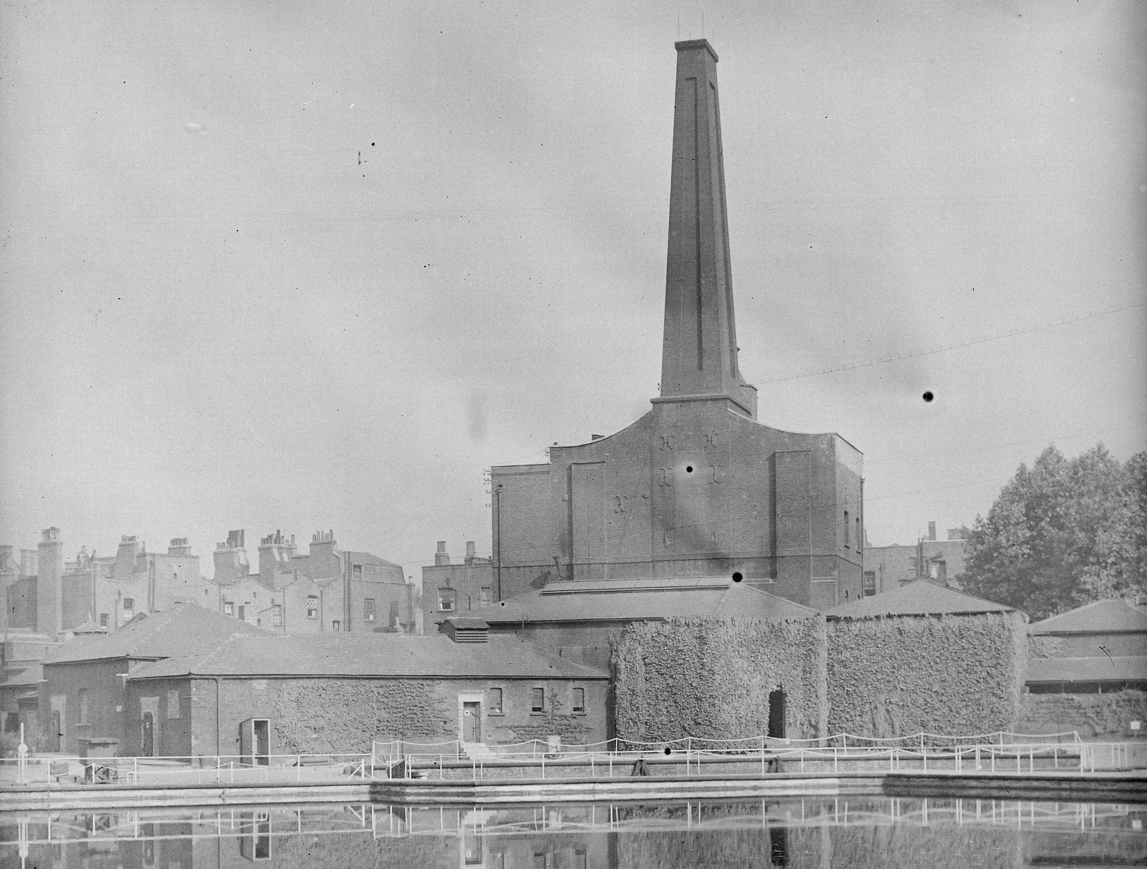 Black and white photograph of industrial brick buildings reflected in a pond in the foreground