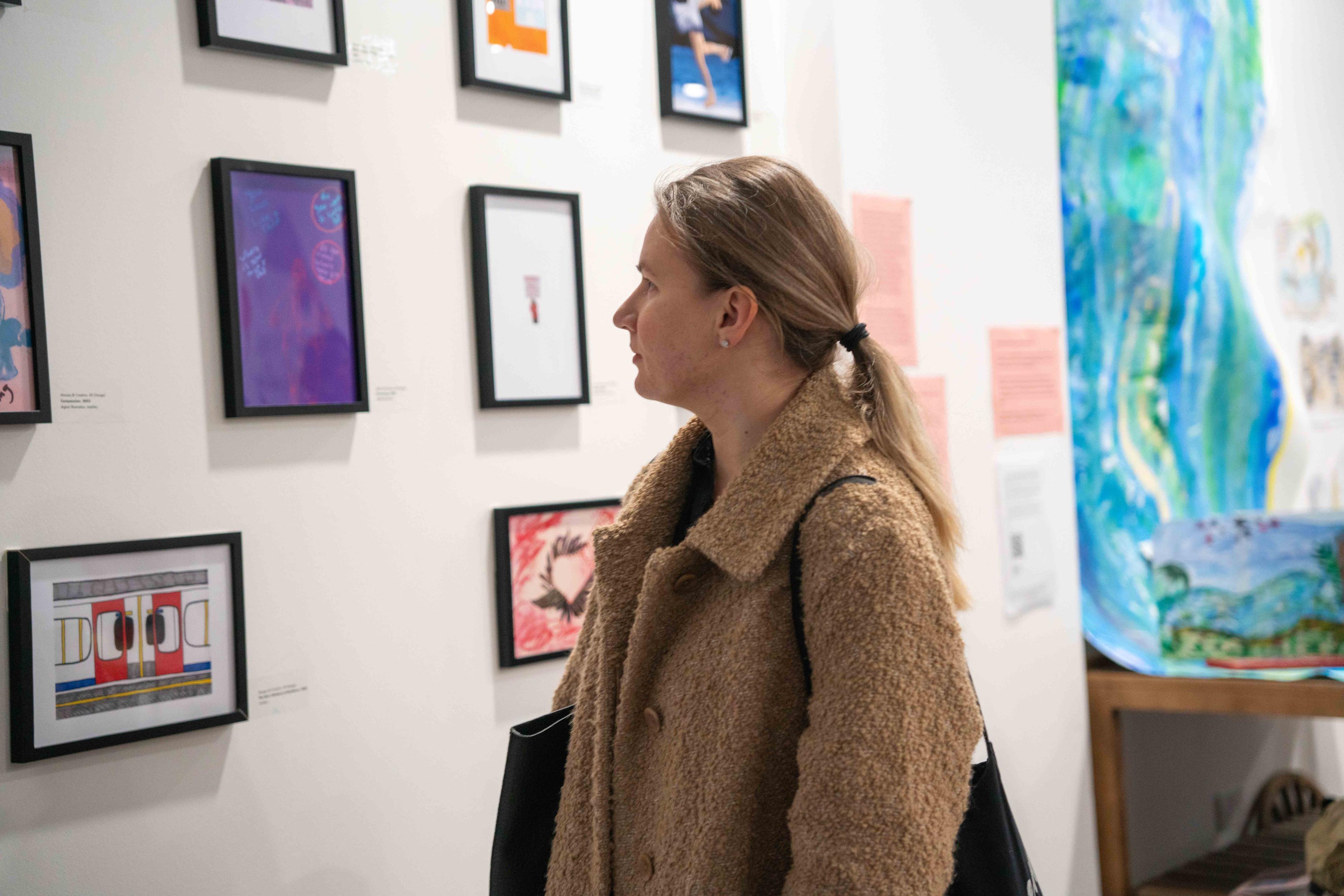 Person looking at illustrations framed and displayed on a white wall.