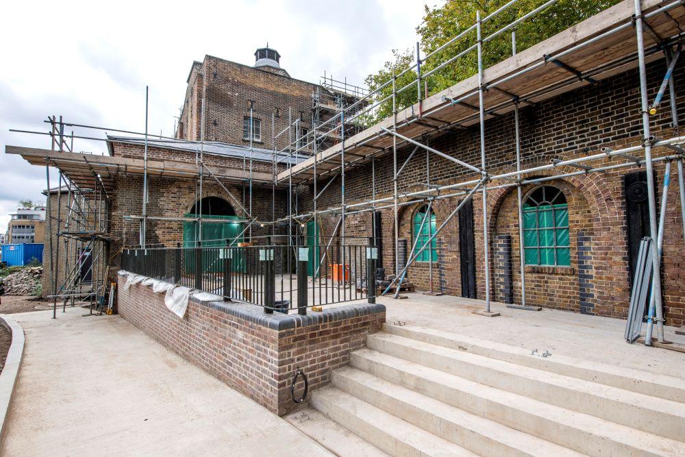 Brick building with steps under renovation, covered in scaffolding.