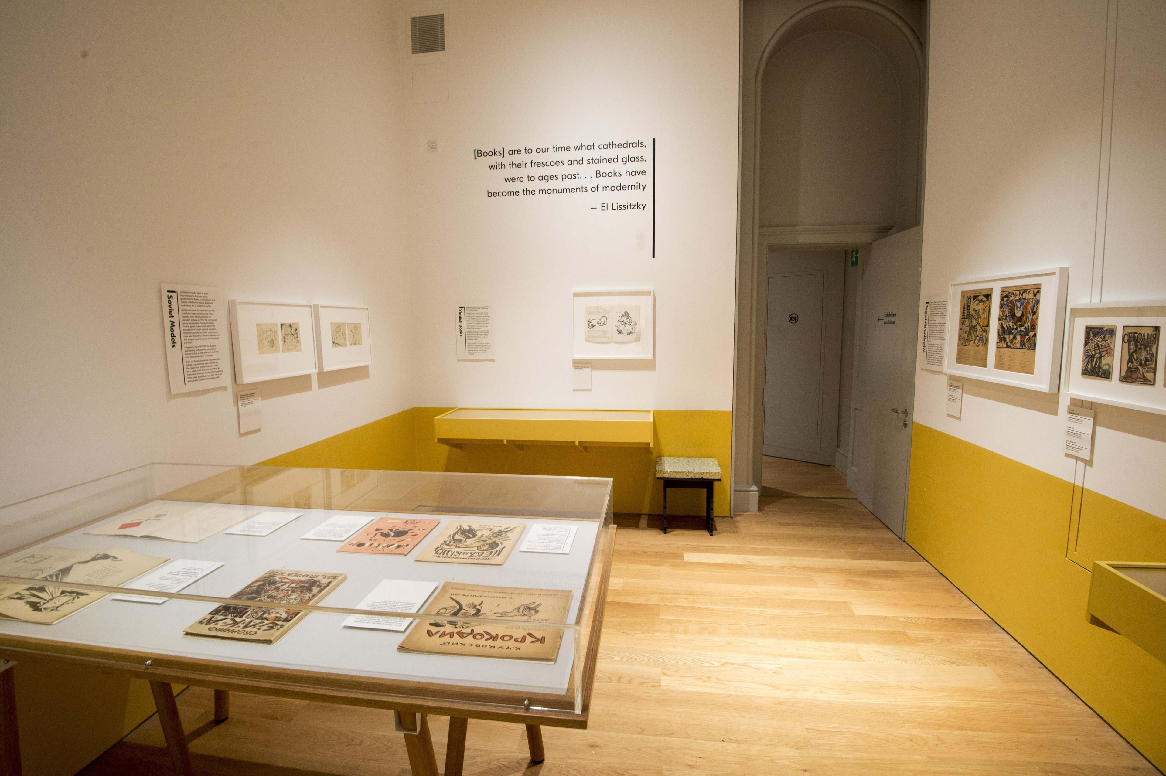 Inside an exhibition space with framed illustrations on the wall and displayed in a glass cabinet.