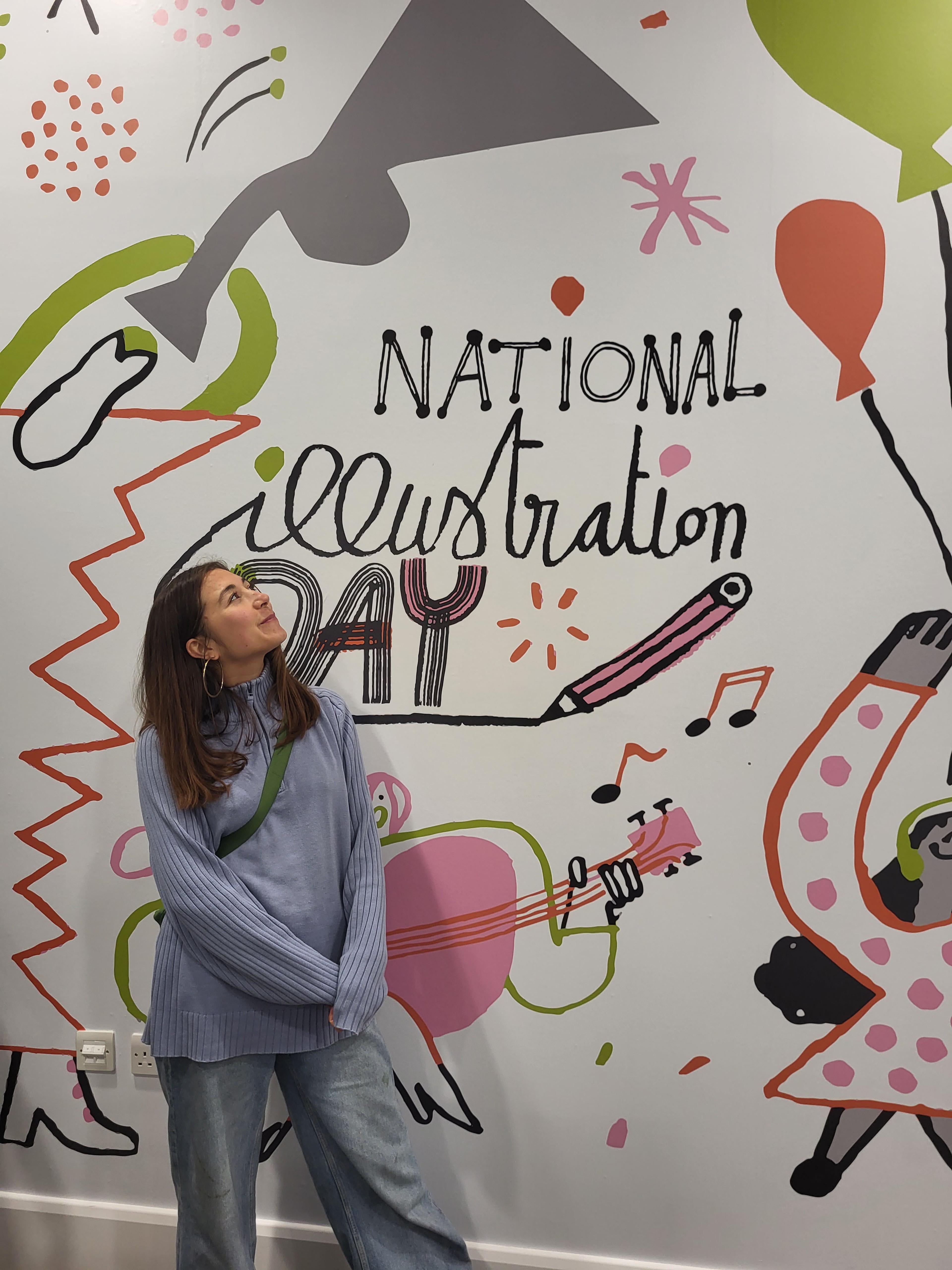 Person standing in front of illustrated wallpaper with the wording 'National Illustration Day'.