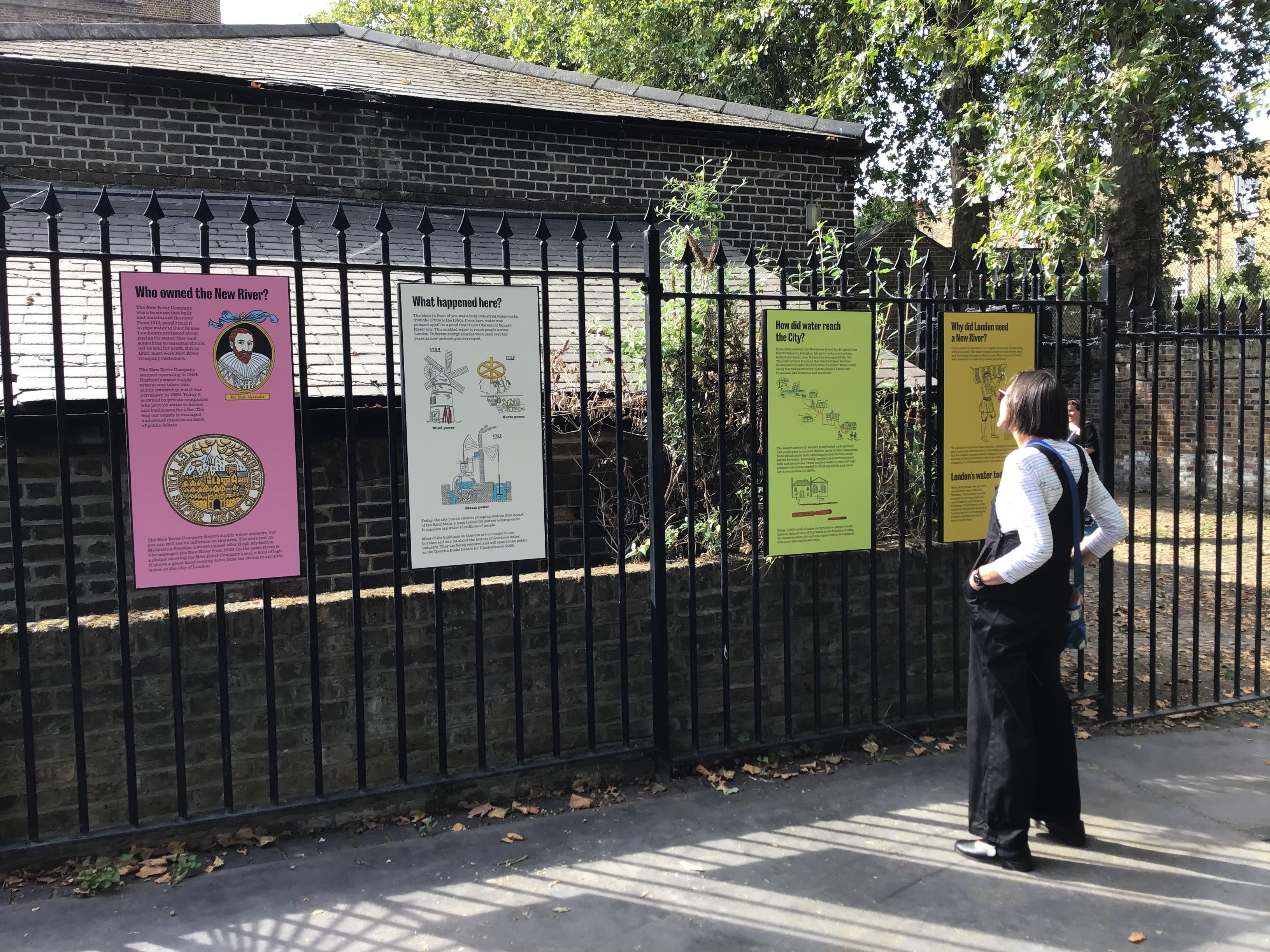 A visitor in a black jumpsuit reading the colourful panels featuring text and illustrations shedding light on the history of New River Head.