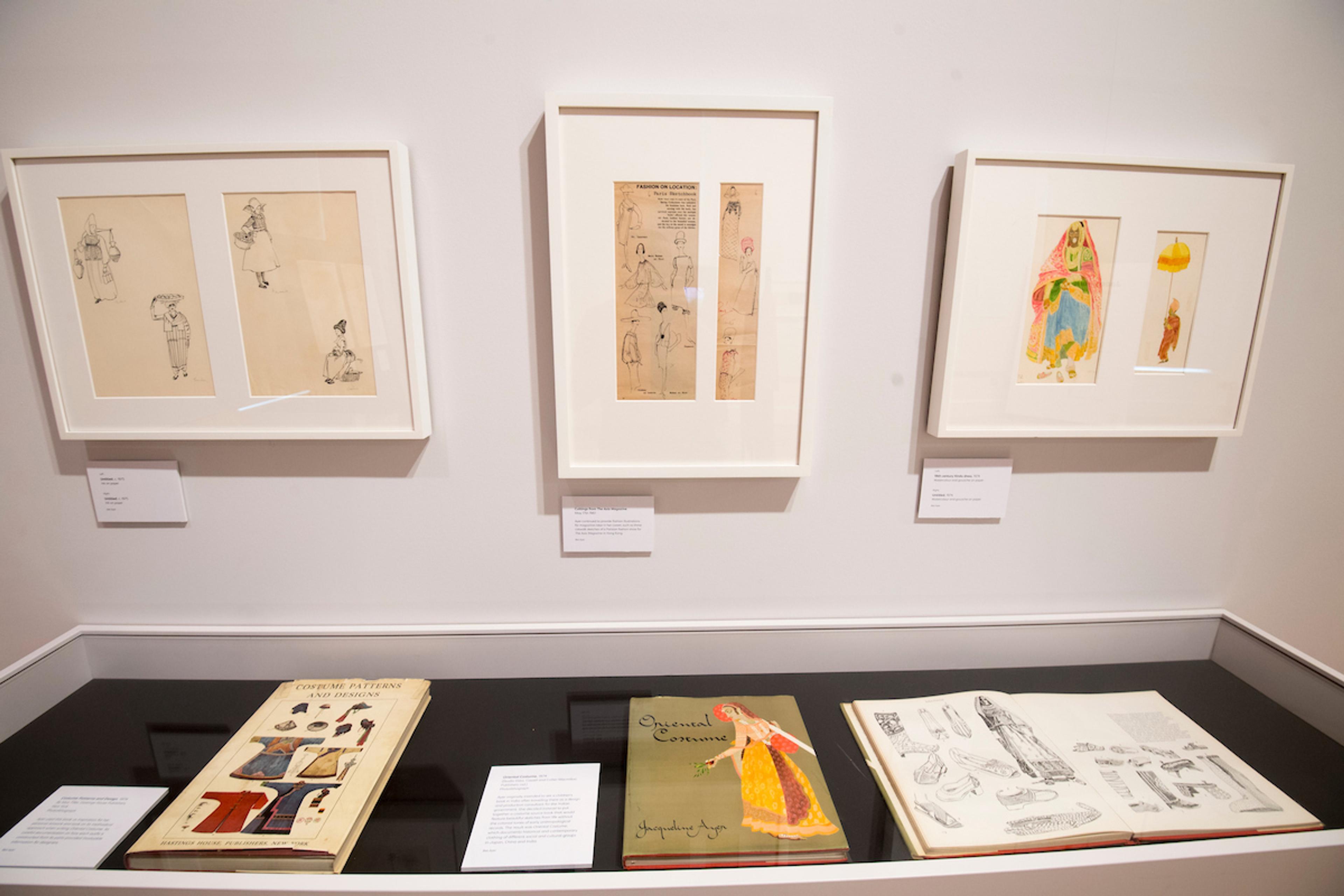 Inside an exhibition space with framed illustrations on the wall and displayed in a glass cabinet.