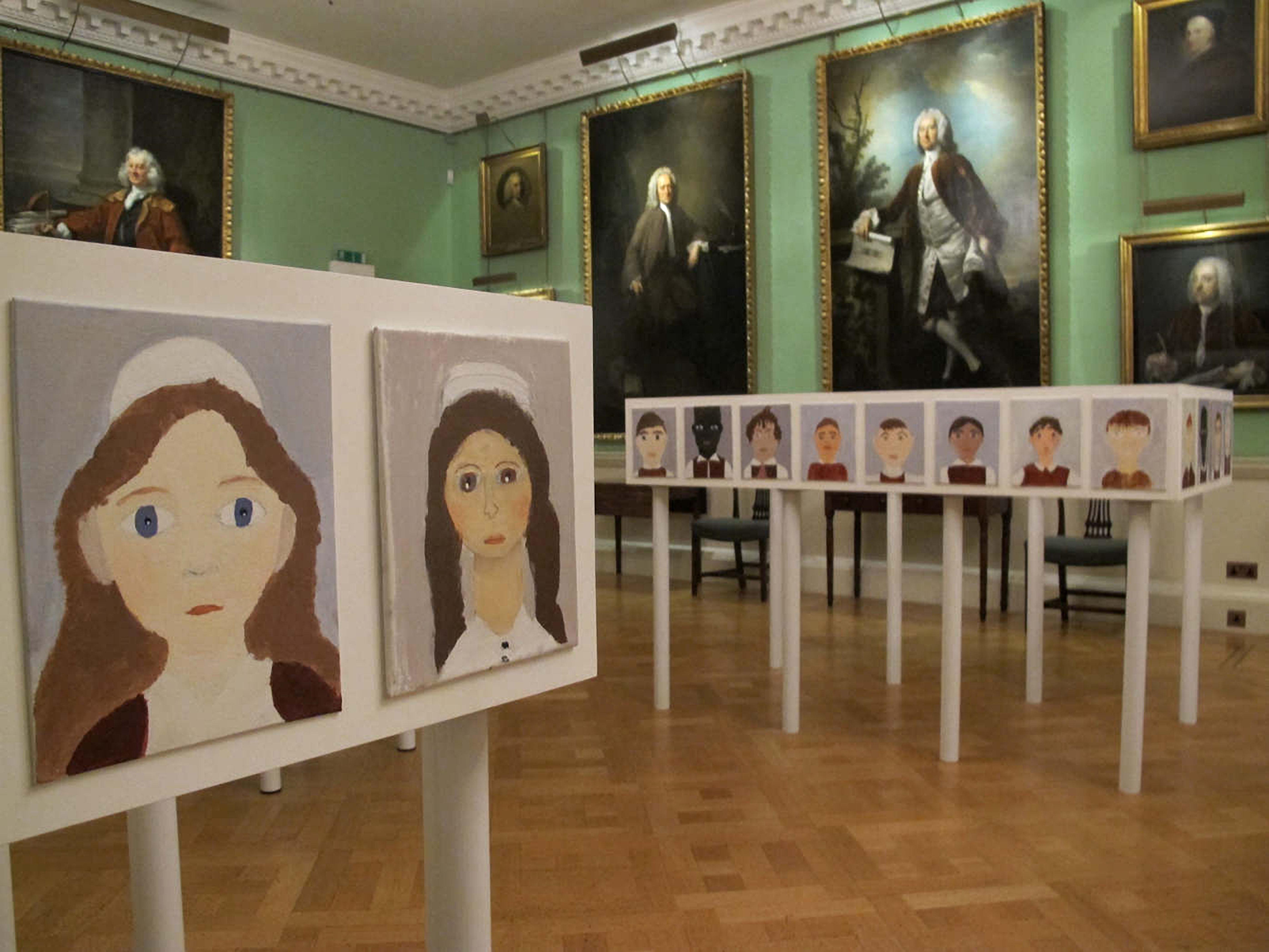 A display of paintings inside a room with very grand decoration including large oil paintings on the wall and a wooden floor.