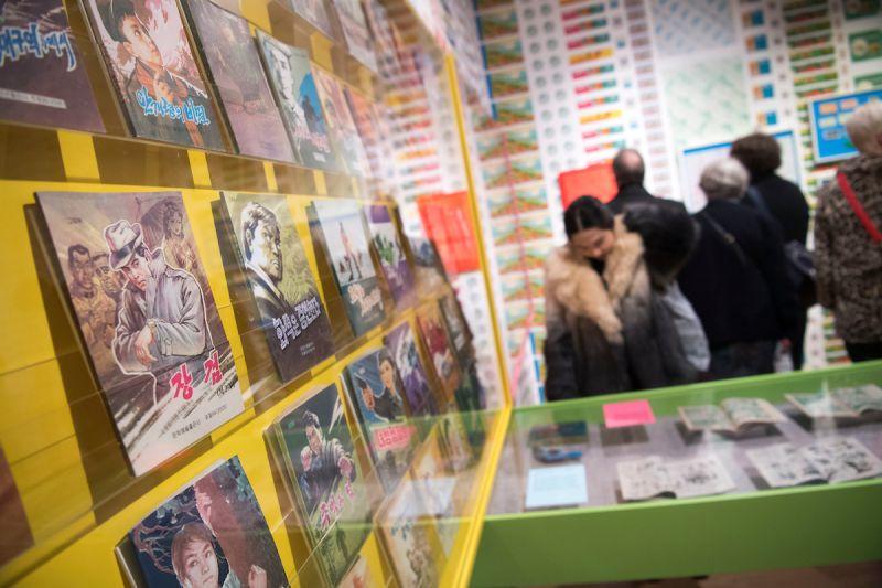 Visitors exploring illustrated books and graphic novels displayed on yellow shelving at a previous Quentin Blake Centre for Illustration exhibition, with colourful illustration collections visible in background.