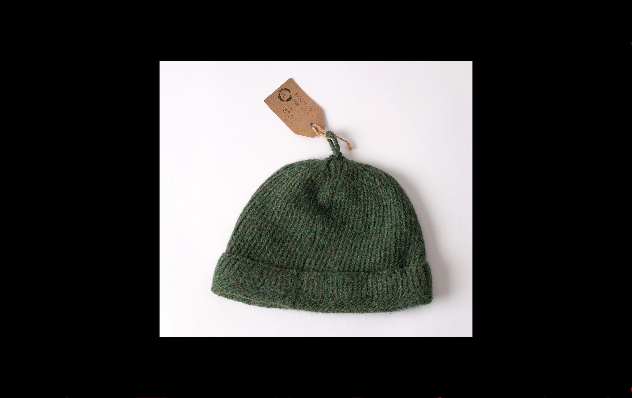 Photograph of a green knitted hat with a museum label attached to a loop at the top