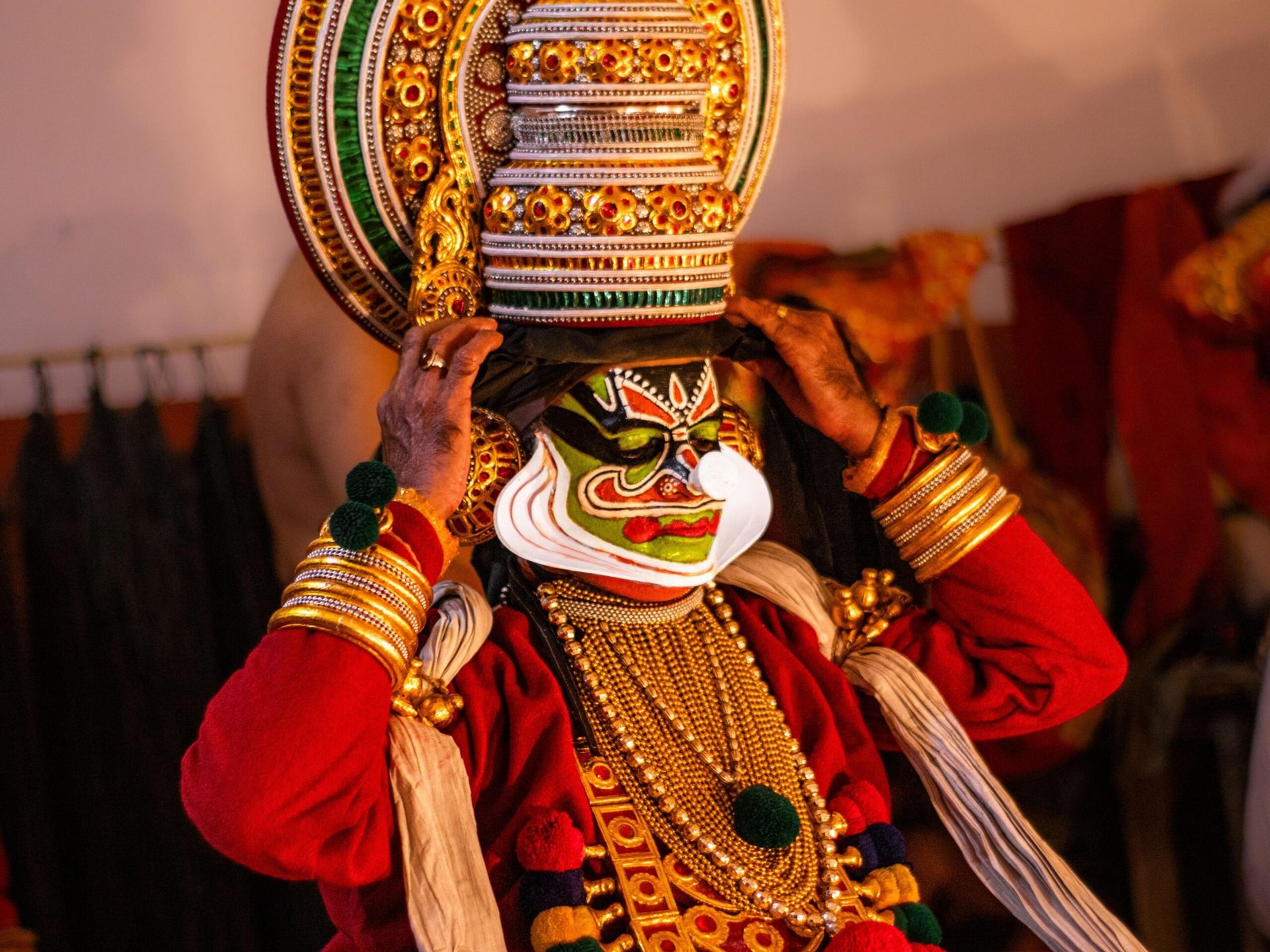A Kathakali performer donning traditional attire and face makeup backstage, capturing the essence of Indian classical dance.