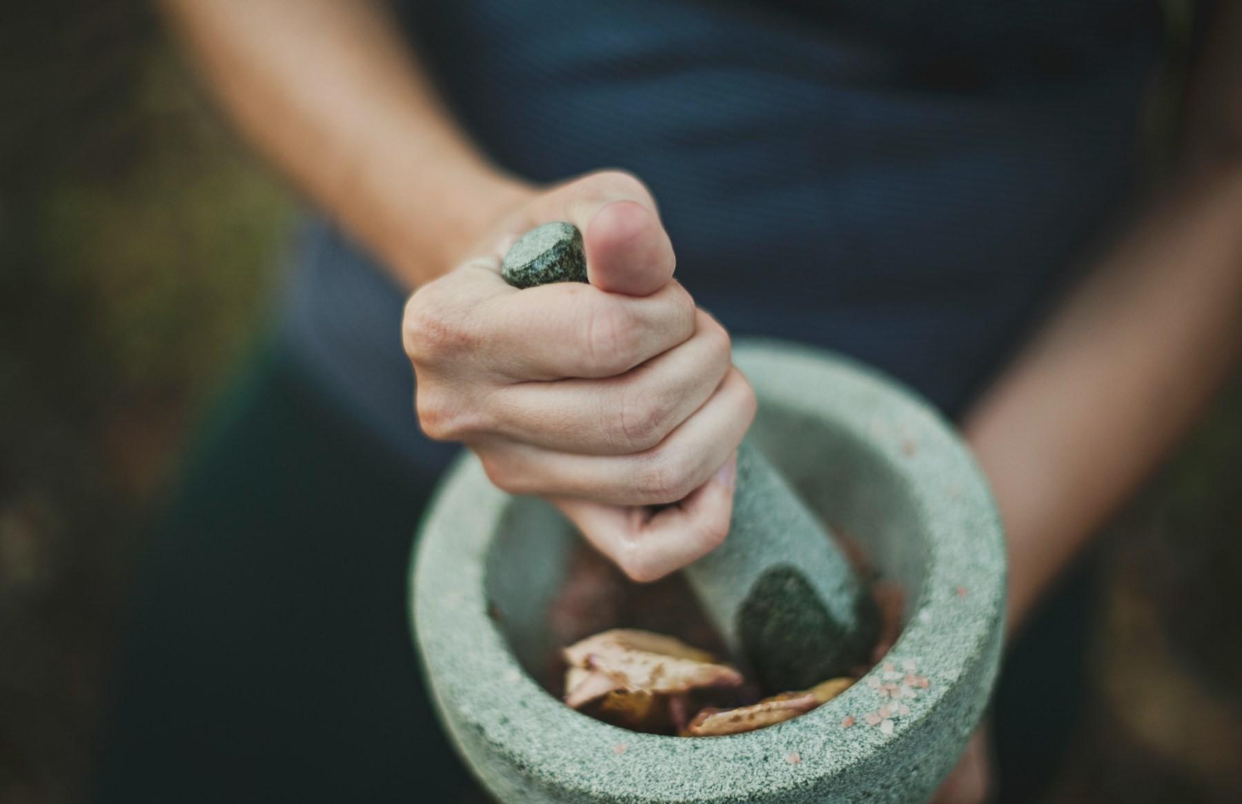 Herbs being ground in a stone mortar and pestle for an Ayurvedic remedy