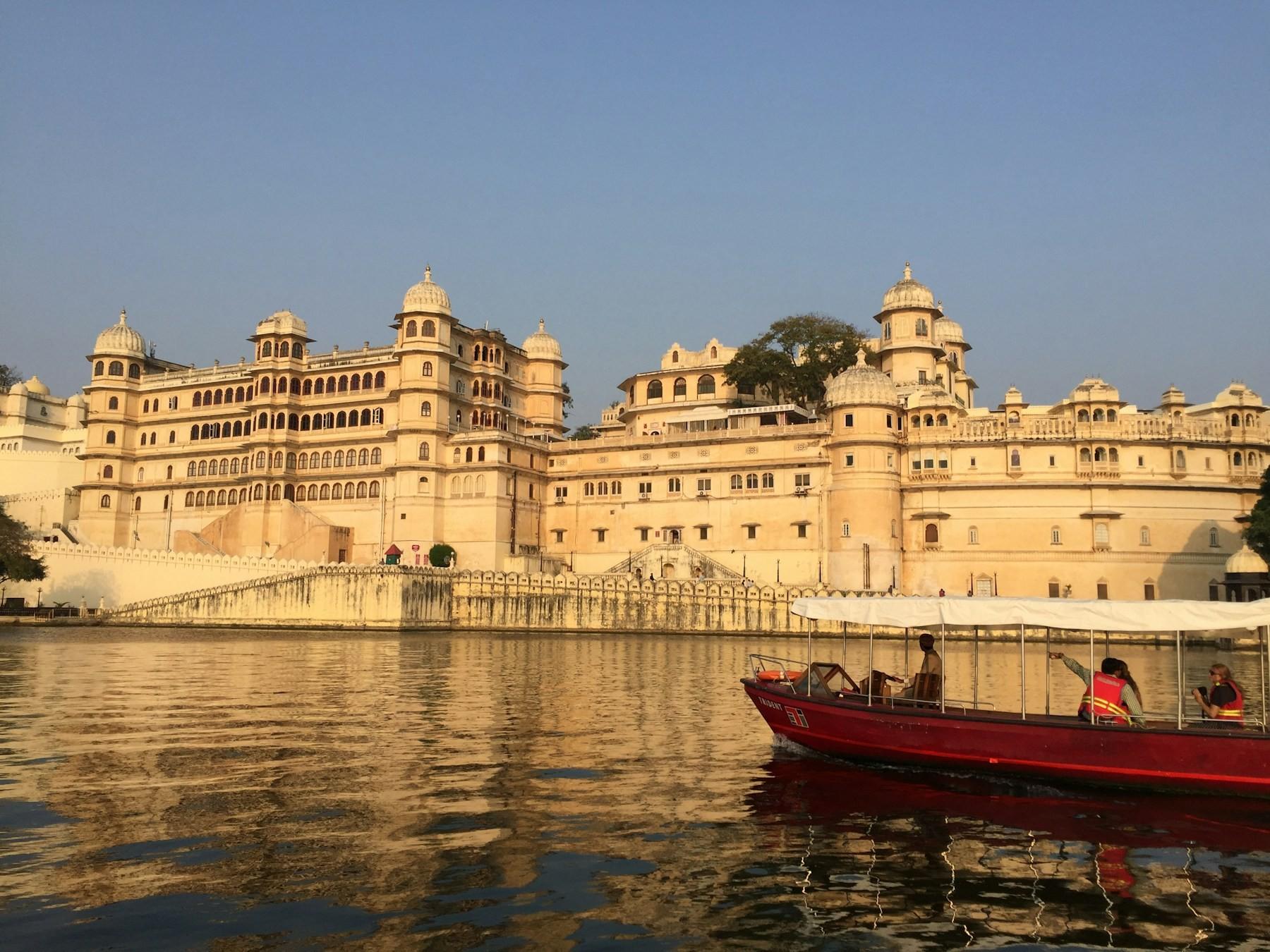 The City Palace of Udaipur above Lake Pichola at golden hour, with a boat on the lake