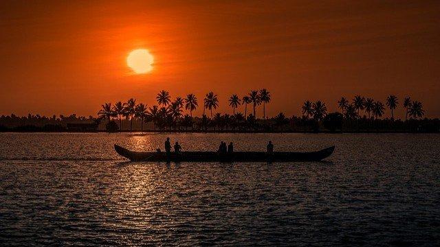 A stunning Kerala backwaters sunset with silhouetted fishermen in a traditional canoe and coconut palms.