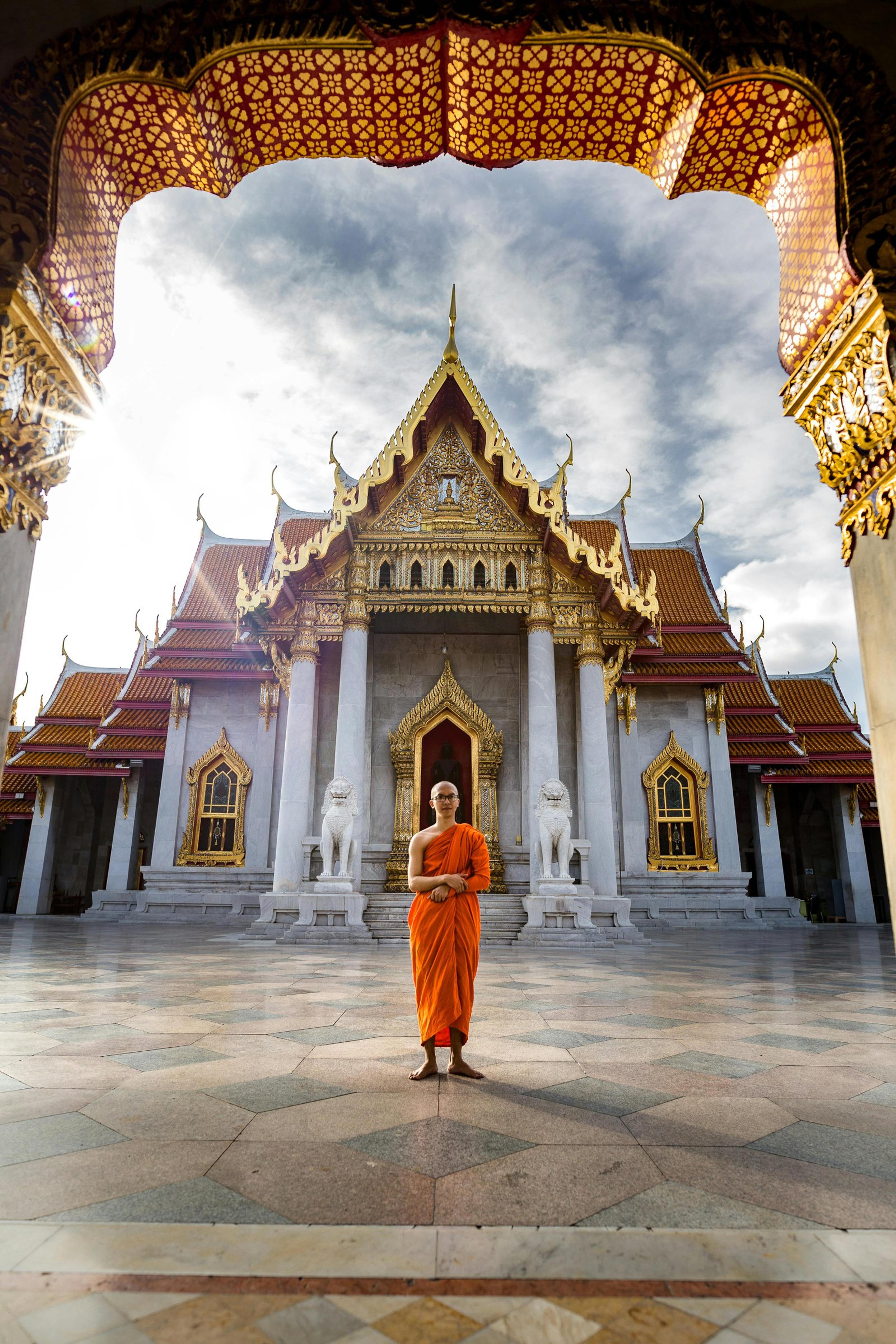 A Buddhist monk standing in front of the iconic Wat Benchamabophit Temple, Bangkok, capturing spiritual tranquility.