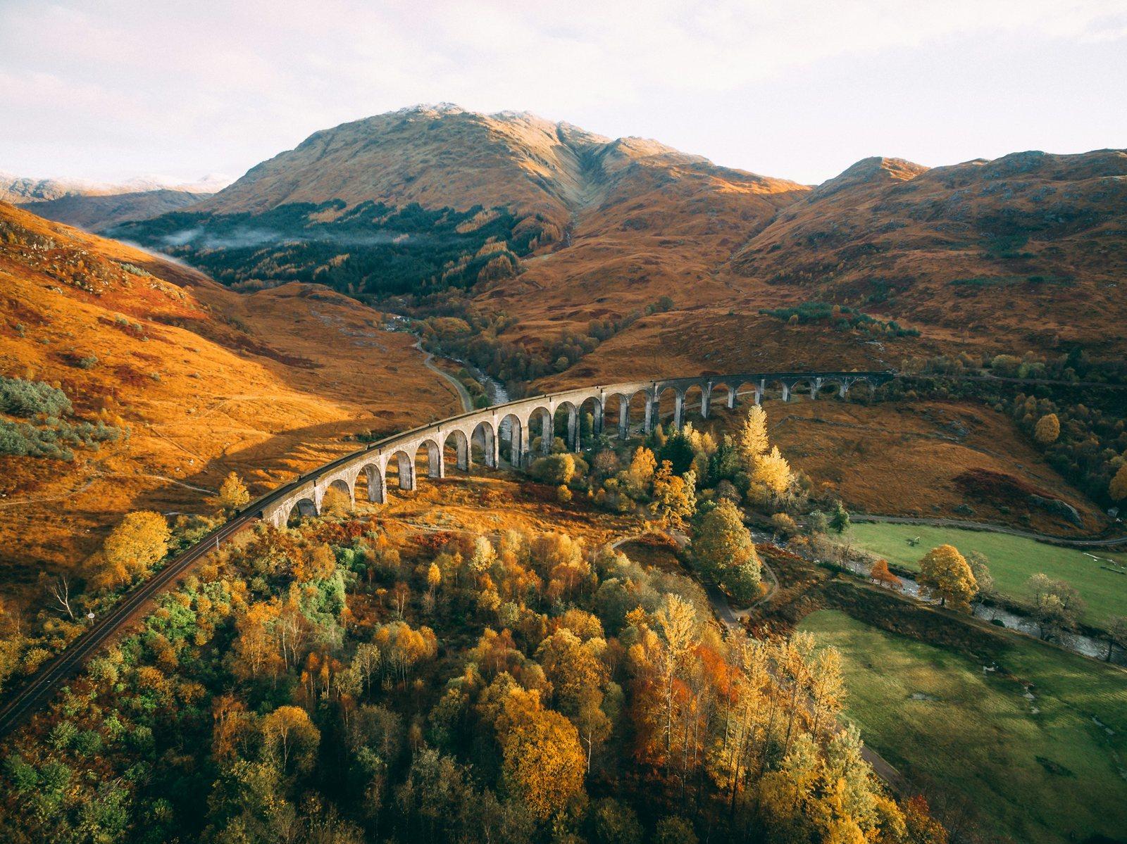 The Glenfinnan Viaduct curving through autumn-gold Scottish Highlands, the 'Harry Potter' railway bridge near Fort William