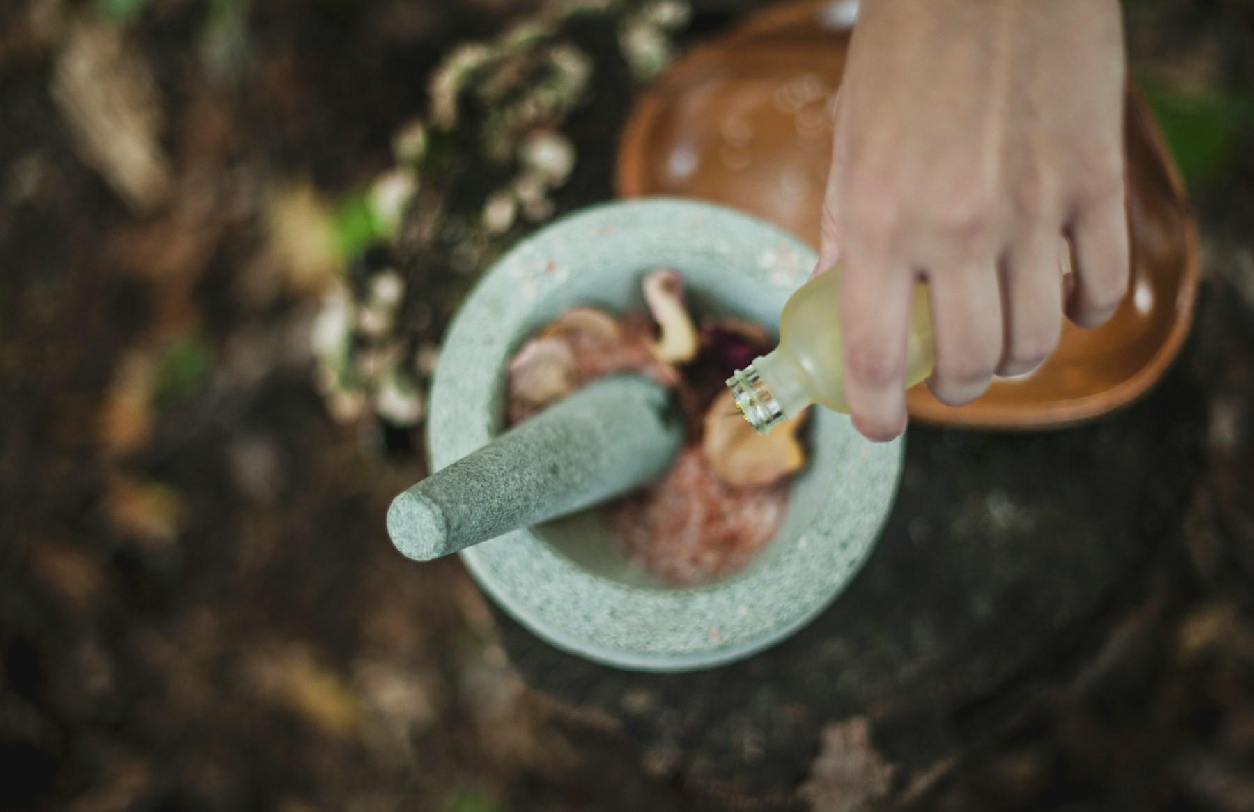 Herbal oil being poured into a stone mortar for an Ayurvedic preparation
