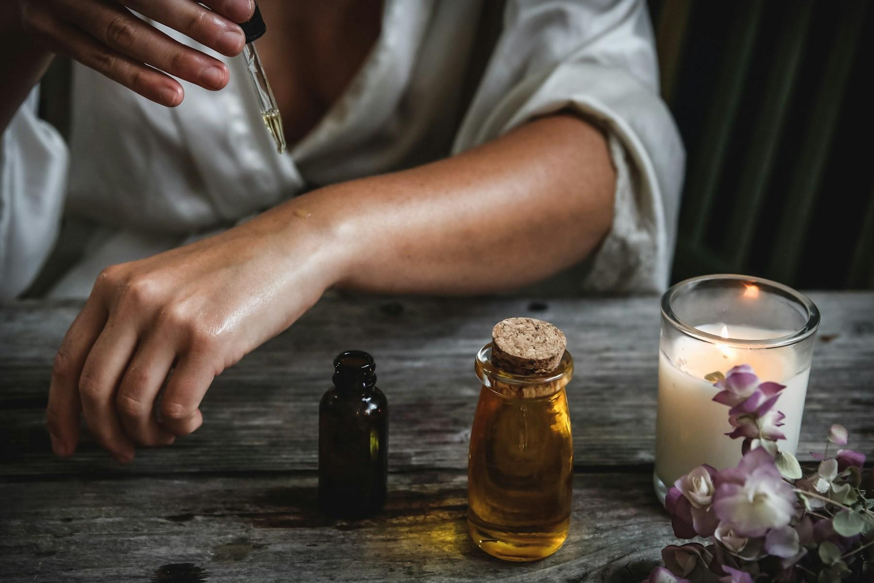 A therapist applying Ayurvedic oil from a dropper beside bottles of herbal oil