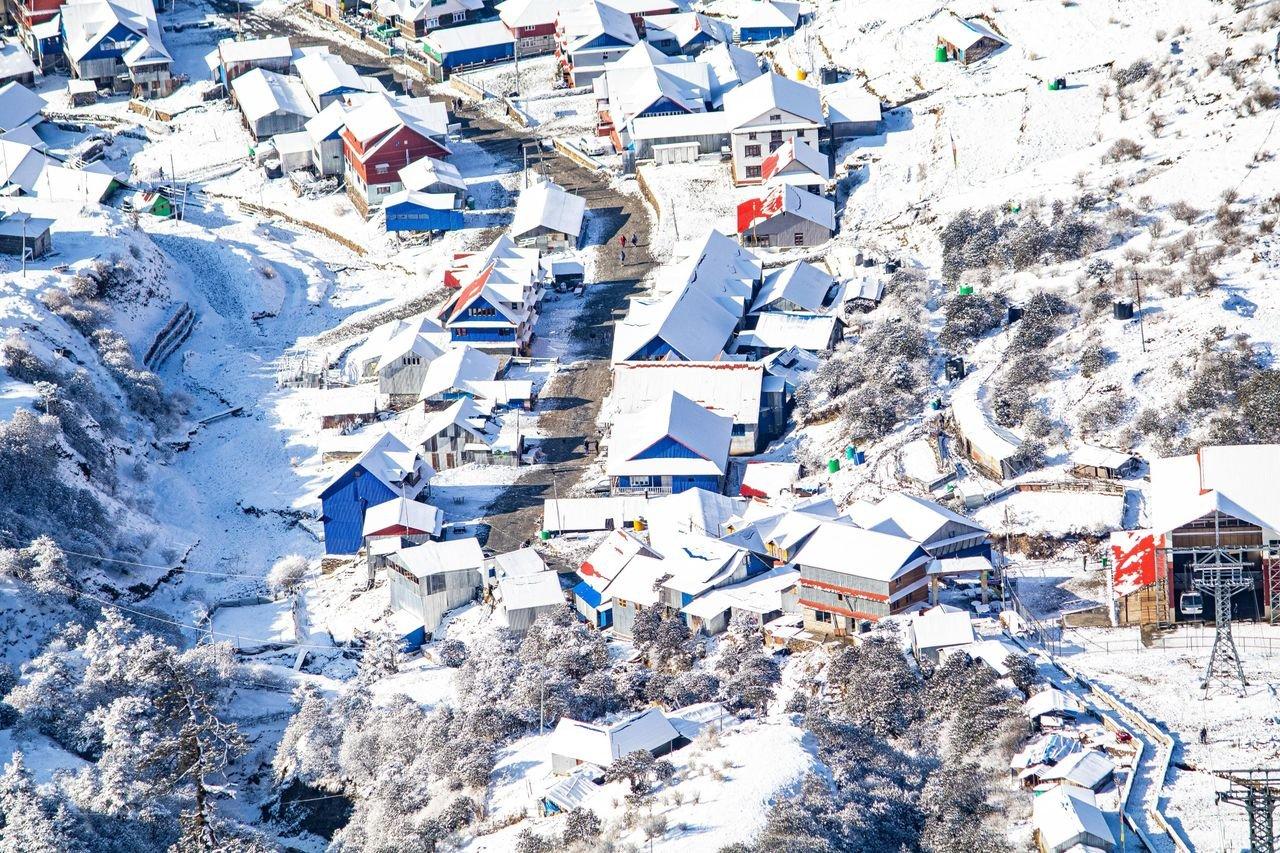 Aerial shot of a snow-covered mountain village with colorful roofs, creating a picturesque winter scene.