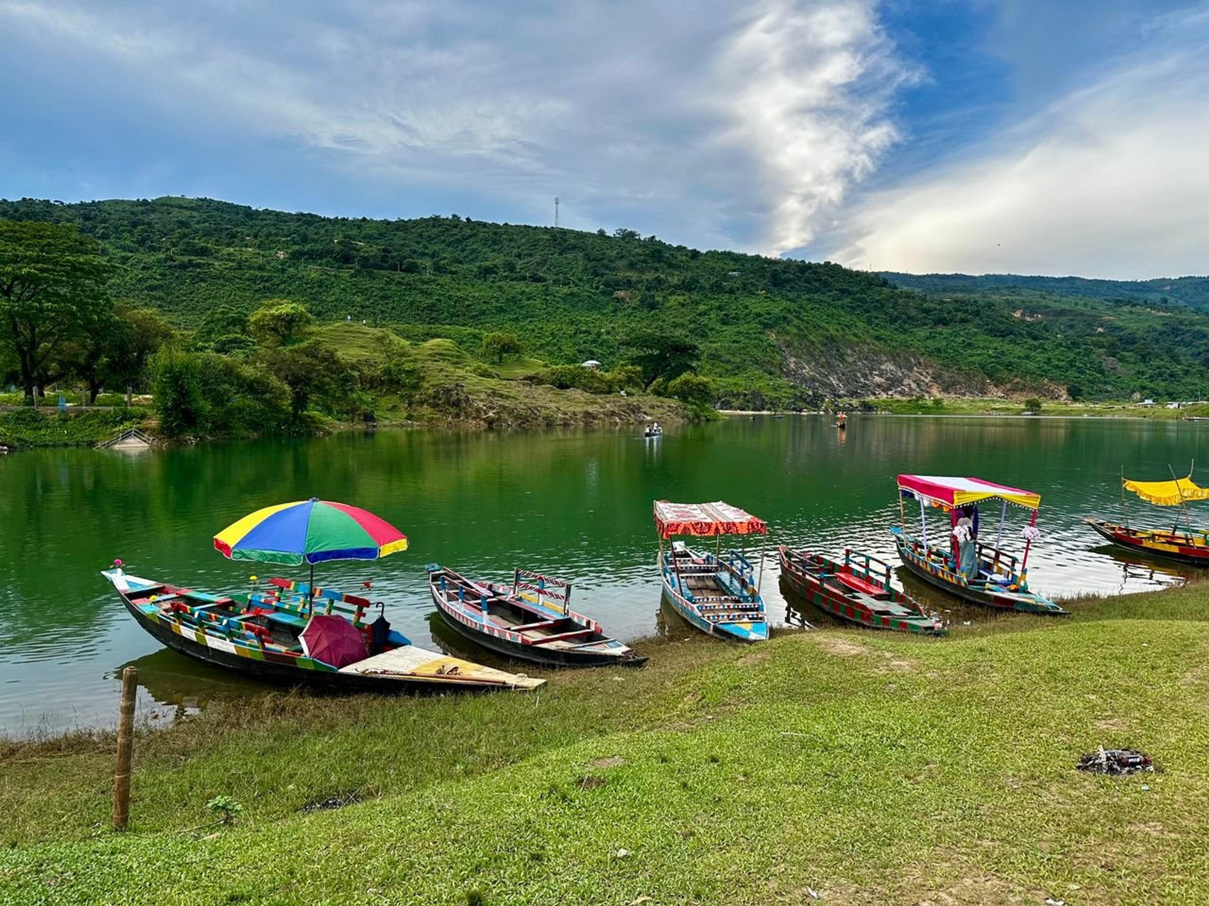Vibrant wooden boats floating on a serene lake with lush green hills in Meghalaya, India.