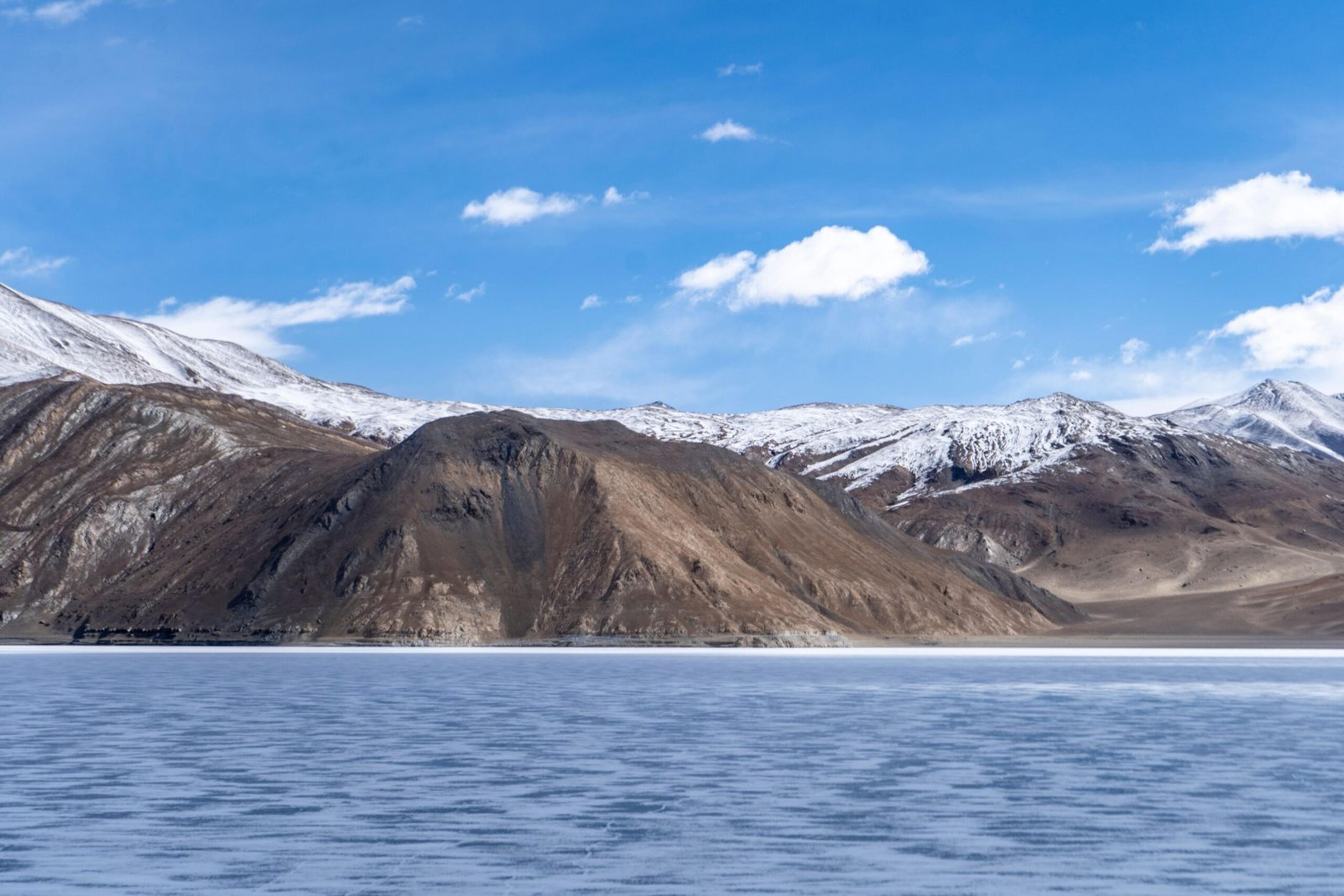 Beautiful snow-capped mountains with a frozen lake under a clear blue sky.