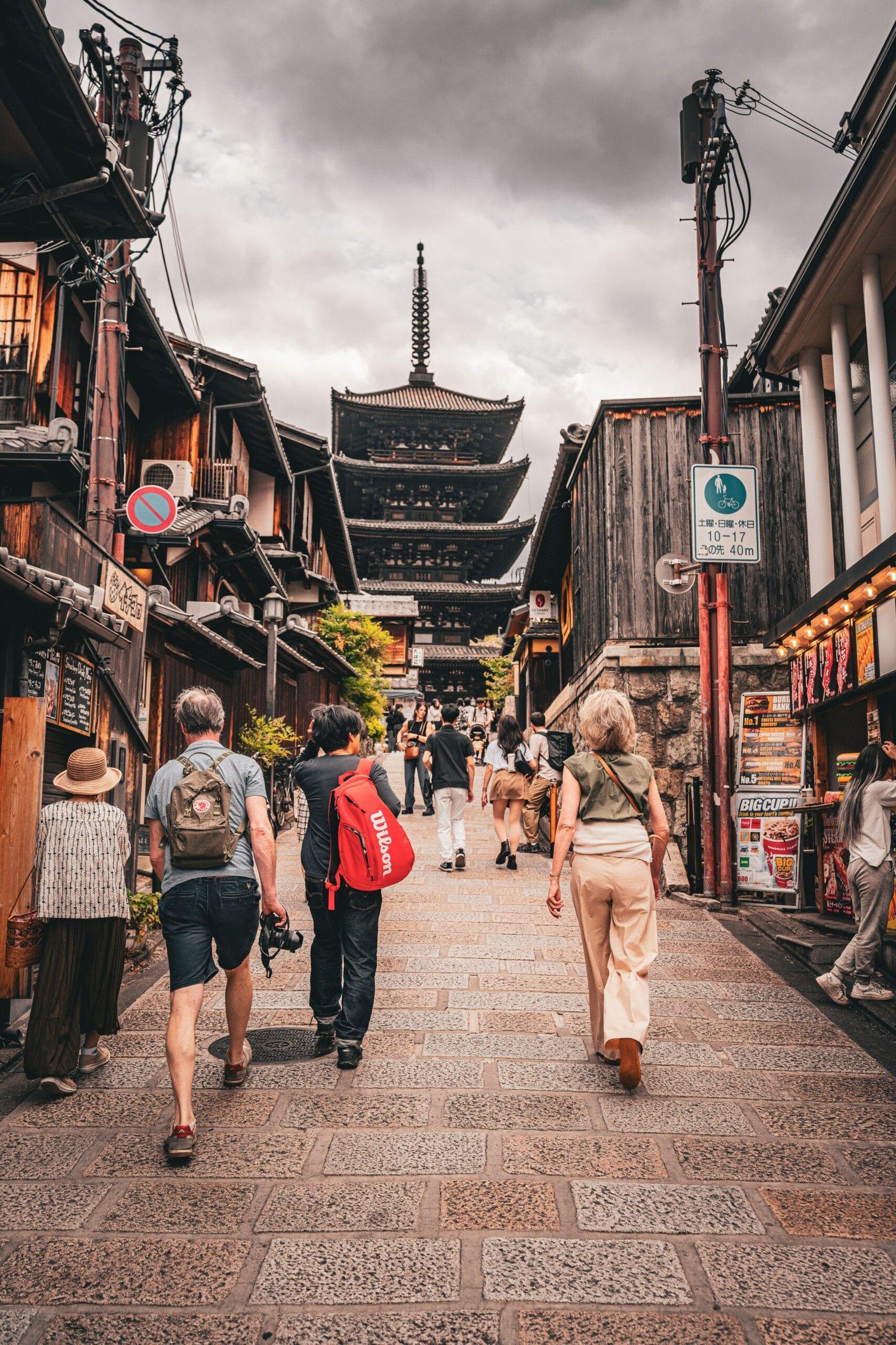 Tourists stroll down a historic street towards the iconic Yasaka Pagoda in Kyoto, Japan, showcasing traditional architecture.