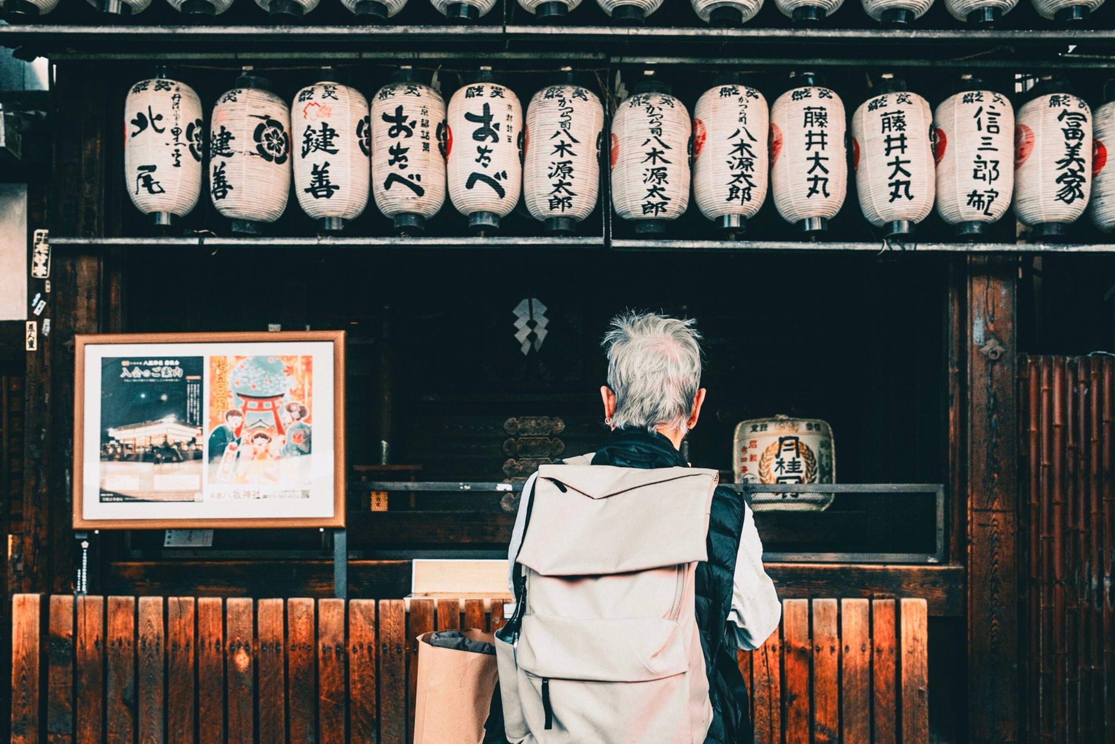 Back view of traveler with backpack looking at hanging Japanese lanterns outdoors.