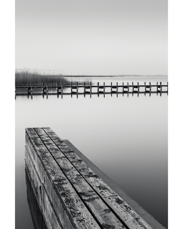 Wooden pier reflected in calm black and white water