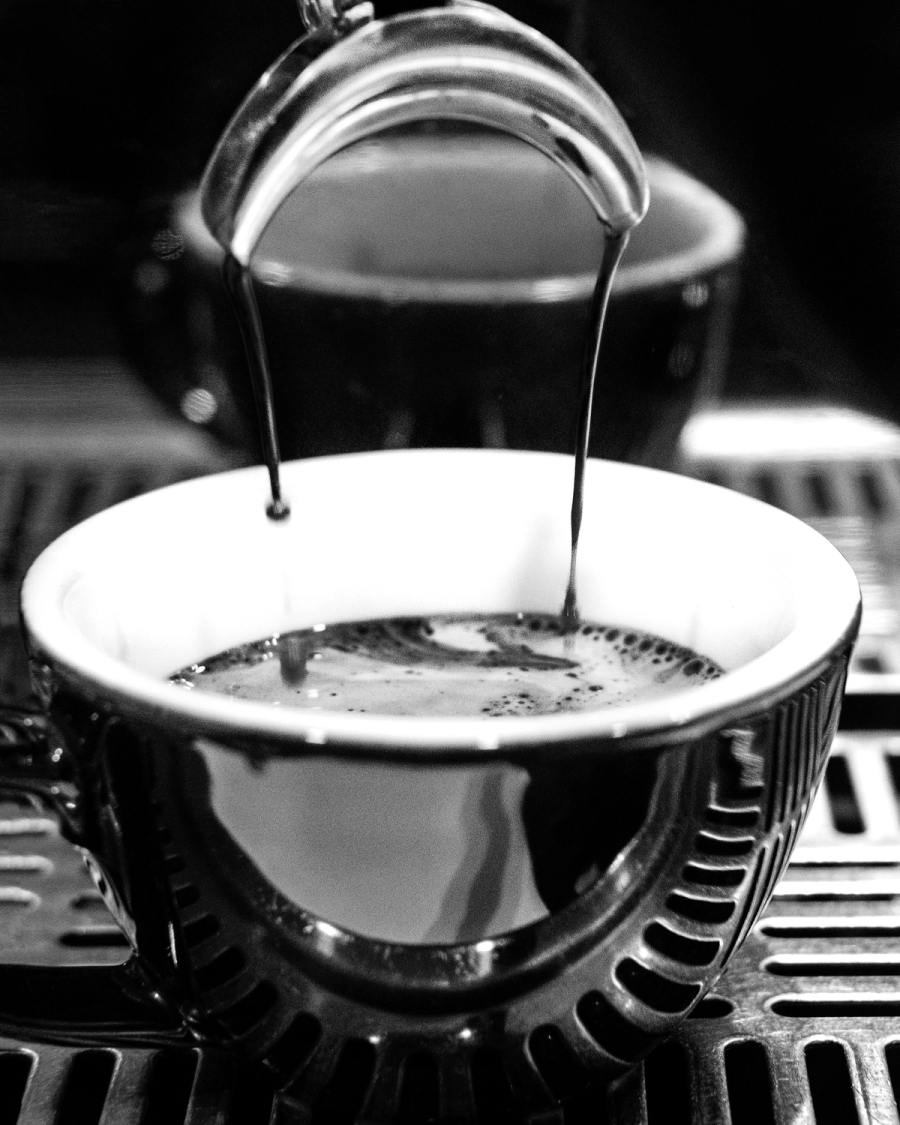 Black and white photo of espresso pouring from a machine into a white cup with crema on top