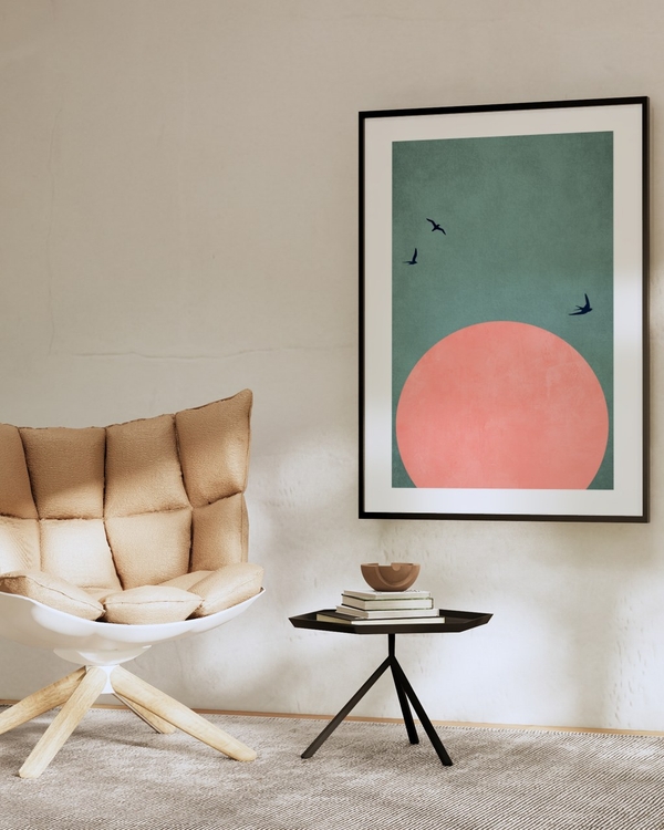 Coral Sun Flight poster in a slim black frame on a beige plaster wall above a dark side table