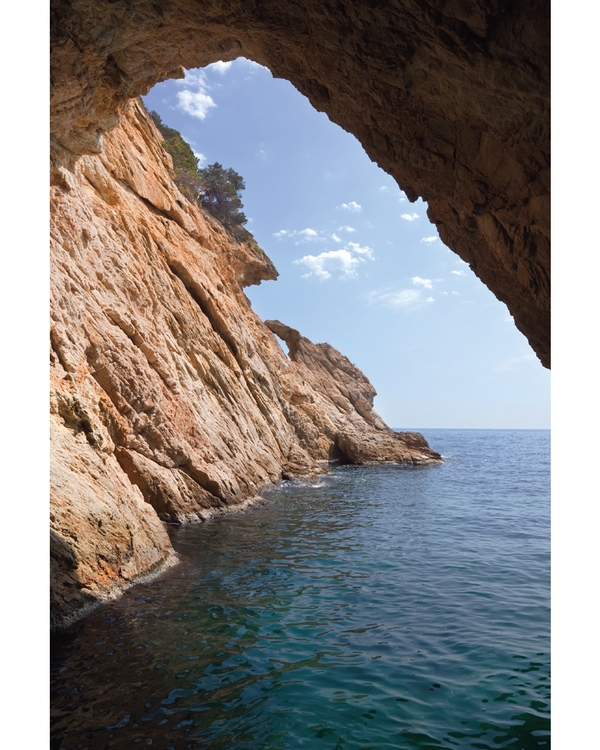 Rocky coastal cave opening toward calm blue sea