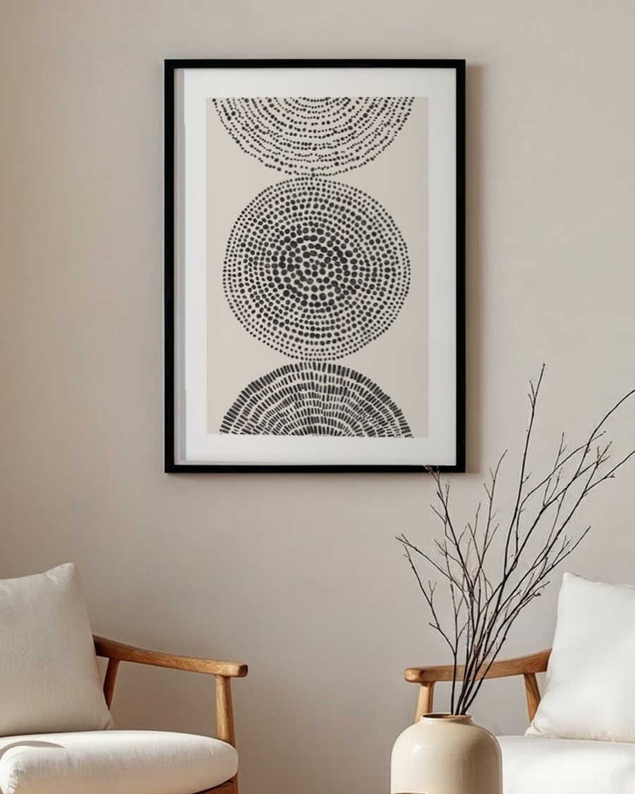 Stippled Circles poster in a slim black frame above two wooden armchairs in a neutral living room