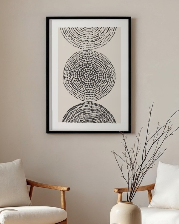 Stippled Circles poster in a slim black frame above two wooden armchairs in a neutral living room