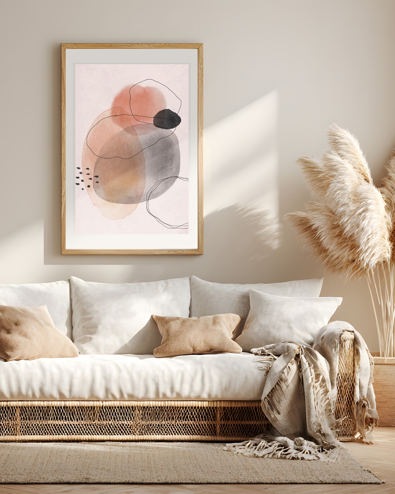 Abstract poster with terracotta, gray and black organic shapes in a light wood frame above a white rattan sofa