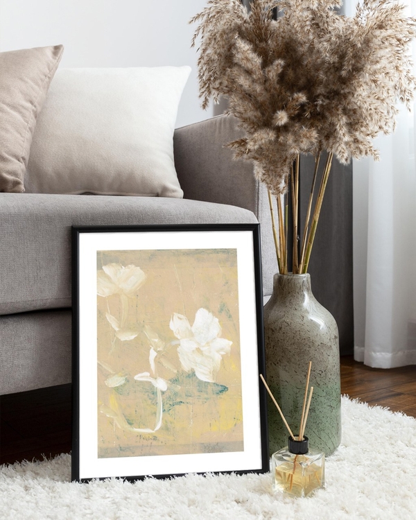 Painted Ivory Blooms poster in a slim black frame leaning on a fluffy rug beside a grey sofa