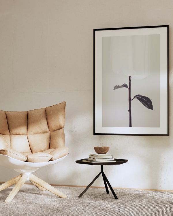 Veiled Bloom poster in a slim black frame on a beige plaster wall above a dark side table