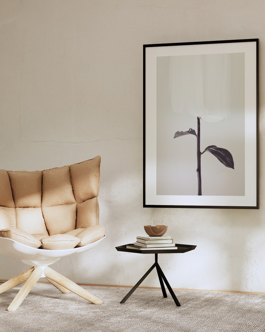 Veiled Bloom poster in a slim black frame on a beige plaster wall above a dark side table