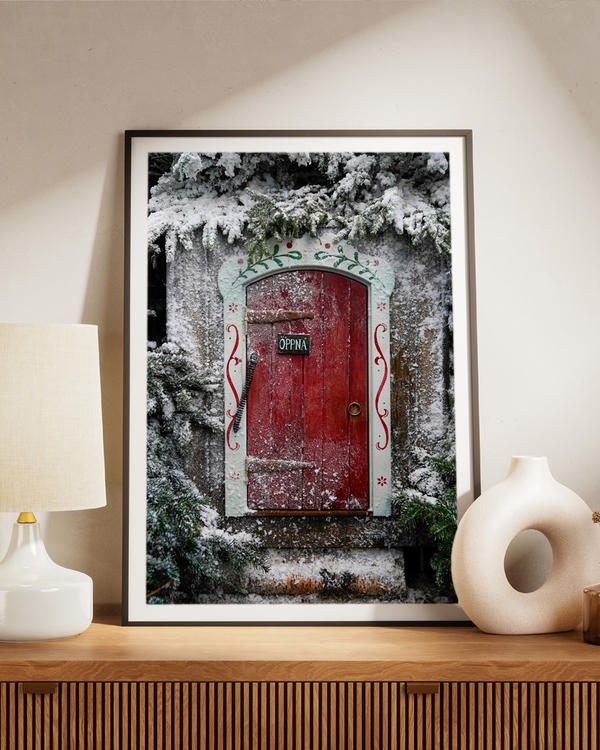 A poster of A vibrant red doorway framed by frosted evergreens and Nordic folk art
