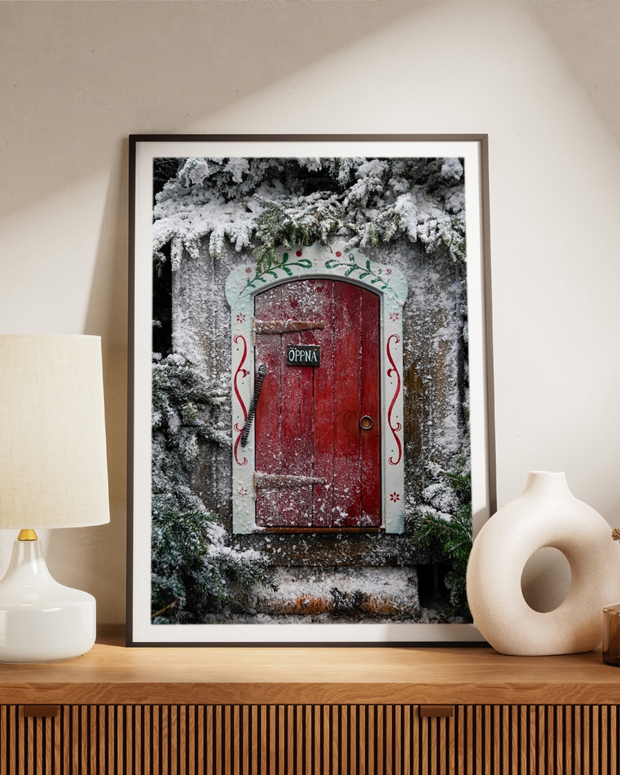 A poster of A vibrant red doorway framed by frosted evergreens and Nordic folk art