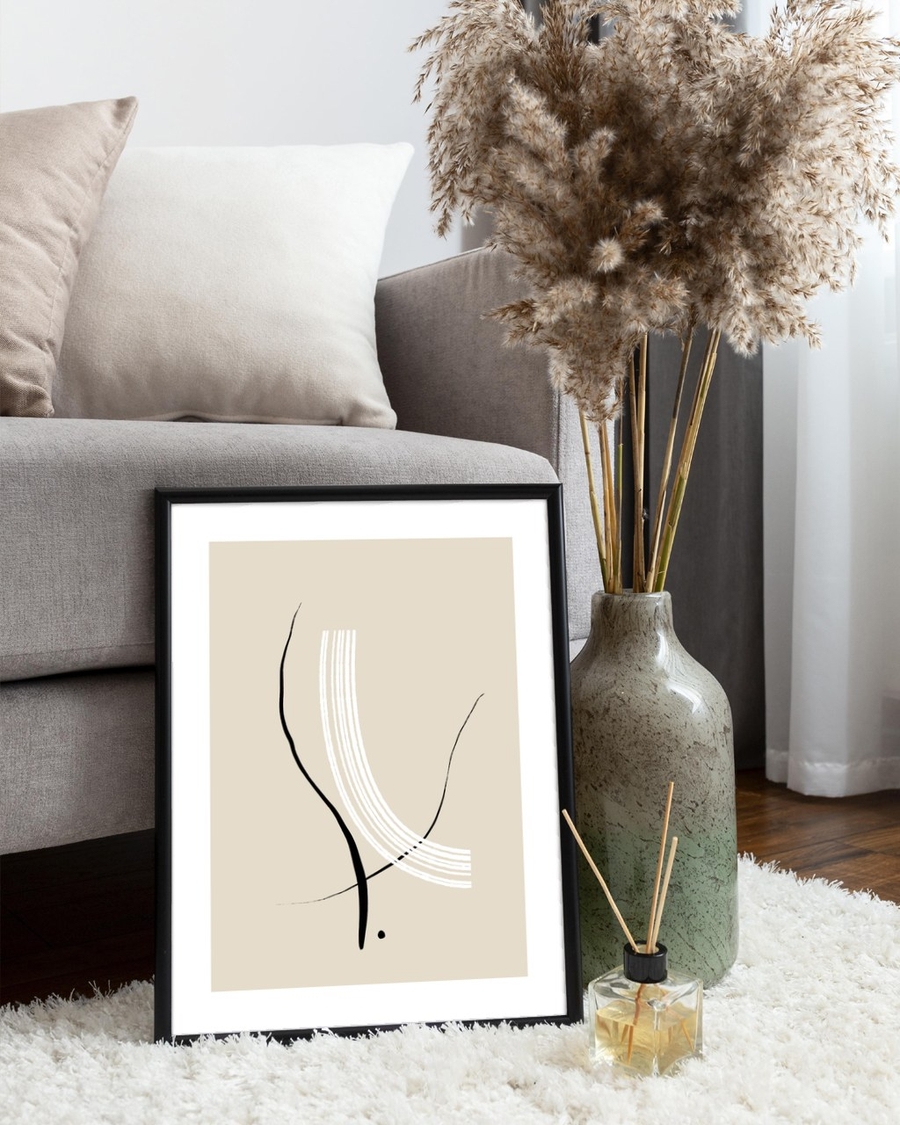 Ink and Ivory poster in a slim black frame leaning on a fluffy rug beside a grey sofa