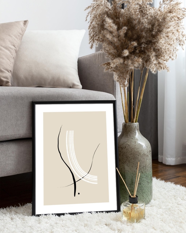 Ink and Ivory poster in a slim black frame leaning on a fluffy rug beside a grey sofa