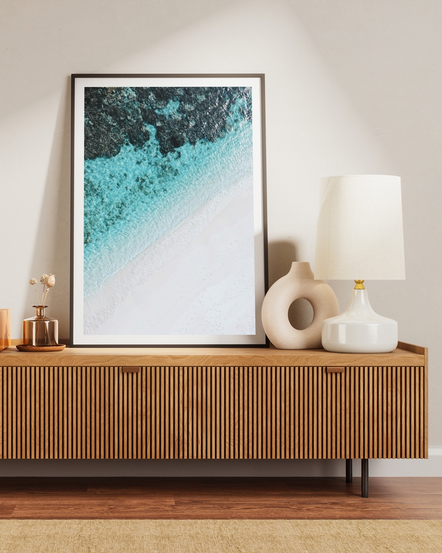A poster of a tranquil aerial view of turquoise waves meeting soft white sand placed on a brown table