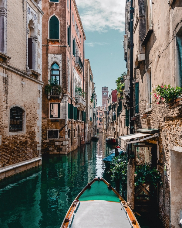 Photo from a boat looking down a narrow Venice canal with green water, brick facades and a bell tower